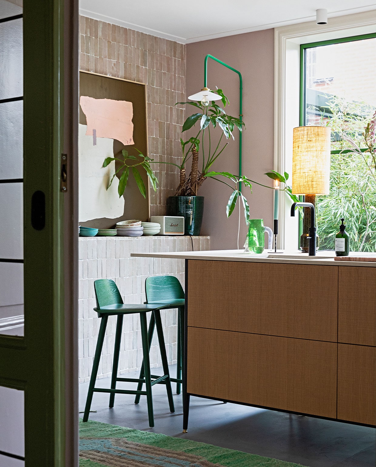 Groene lamp aan muur Valerie Objects. Tegels Bejmat Gris rose Marokkaanse tegels via Design Tegels. Schemerlamp en kunst HKliving. Kandelaar Hema. Kan Hay. Plantenpot Serax. Muziekbox Marshall. Servies mix van onder andere Home Chef en 70’s ceramics van HKliving. Krukken Nerd van Muuto. Keuken Unit van Cesar Kitchens. Kleed vintage berber. Aluminium pui in kleur Varen Groen. Lamp plafond onbekend. vtwonen 04-2022 | styling Ilona Jongepier | fotografie Dana van Leeuwen | visagie Djolien de Kreij