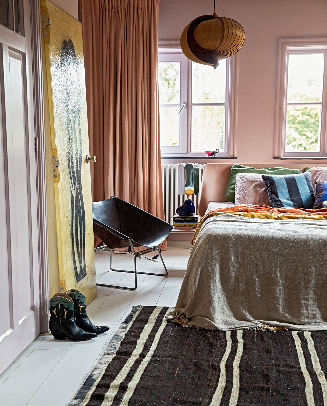 Verf wand Peach Blossom van Little Greene. Gordijnen Soft Salmon Amor Linnen van Vadain. Fauteuil Midcentury design van Pierre Paulin Polak, plafondlamp vintage Moon van Hans Agne Jakobsson, kunststuk tegen wand Fiberglass Deur Midcentrury via Best Wel Hip. Lamp nachtkastje voet van Ferm Living en kap van Hay. Bed Auping. Sprei HKliving. Kussens bedlinnen van Casa Comodo. Kleed Turks vintage. Laarzen Elena Iachi. Overig onbekend. vtwonen 04-2022 | styling Ilona Jongepier | fotografie Dana van Leeuwen | visagie Djolien de Kreij
