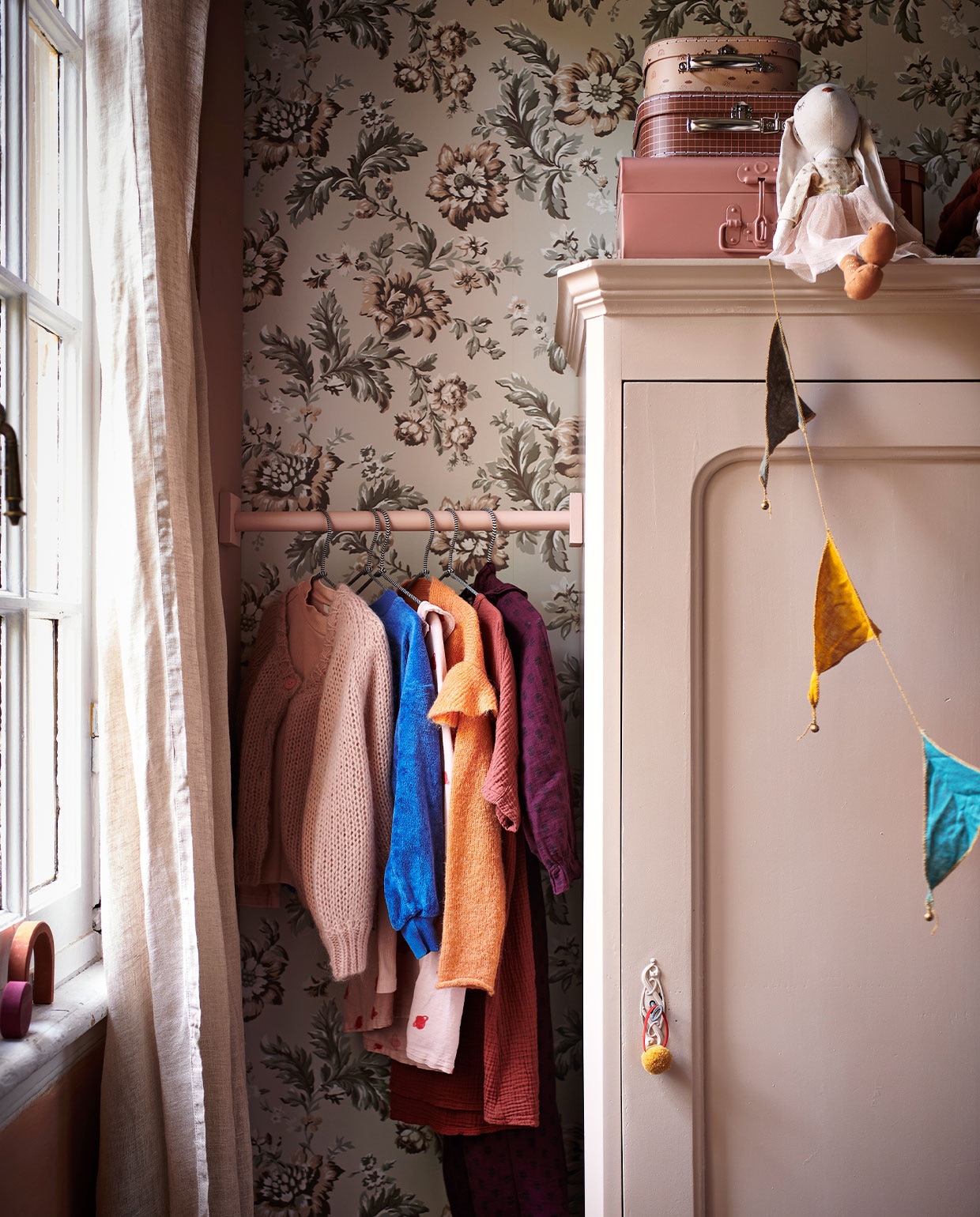 Behang Rosenholm Wheat van Sandberg € 111,56 (sandbergwallpaper.com). Beige linnen gordijnen € 69,99 (hm.com). Lichtroze kast prijs op aanvraag (com-anders.nl). Roze koffer van Bonton € 29,-, set koffertjes met print van Oyoy Living Design € 24,90 (storeofdaydreams.com). Knuffel konijn € 22,99 (zarahome.com). Houten gekleurde blokken van Raduga Grez € 139,- (archive-store.nl). Houten stok geschilderd in de kleur Light Peachblossom (littlegreene.nl). Kleding (fishonthemoon.com). Stoffen slinger multicolour van Numero 74 € 17,- (archive-store.nl). JA vtwonen 13-2021 kids special | styling Kim van Rossenberg | fotografie Sjoerd Eickmans | Assistentie Sanne van der Beek, Judie Jonker, Kim Suos\n