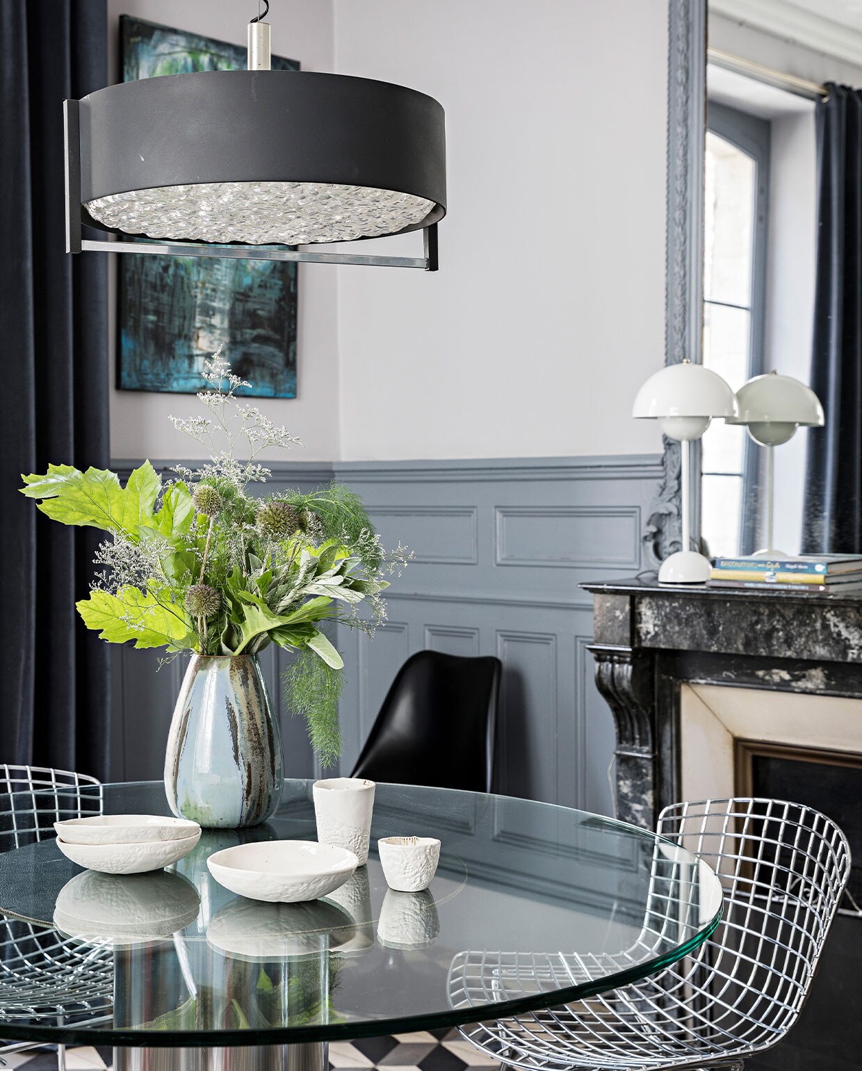 Vintage eettafel van glas en metaal uit 1970, vintage Wire Chairs van Harry Bertoia, jaren 70 hanglamp van onbekende makelij, serviesgoed van Myriam Aït Amar Ceramics, kunstwerk acryl op canvas van Clarisse Friedmann, op de schoorsteen Flowerpot lamp van Verner Panton. De cement- tegels zijn origineel, muurverf van Farrow &amp; Ball. NEE | vtwonen 4-2022 |  styling  Marie-Maud Levron | fotografie Yann Deret | tekst Anne-Catherine Scoffoni | tekstbewerking Chris Muyres
