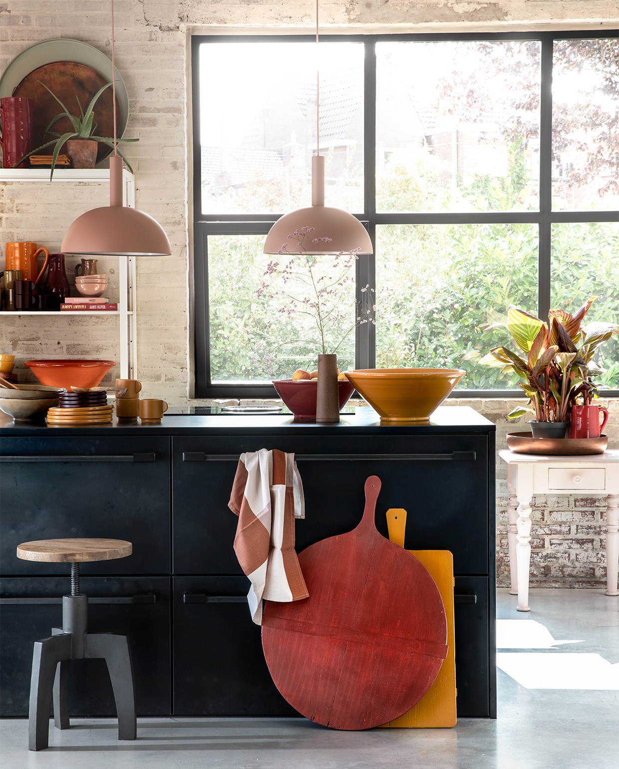 Zachtroze hanglampen Dome Shade van Ferm Living inclusief roze fitting high (vtwonen.nl). Draaikruk Space van BepureHome (Woondock). Grote oude kaasplanken (H&amp;M Home), gelakt met Perfection zijdeglans lak in dieprood en mosterdgeel (Histor). Theedoek okergele kopjes , okergele borden, donkerpaarse borden per stuk (H&amp;M Home). Okergele schaal, donkerrode schaal (In-Petto). Beige schalen (Intratuin). Bovenop de kast: grote donkerrode kan(In-Petto), theedoeken in okergeel en donkerpaars (H&amp;M Home), koper­kleurige schaal van BePureHome , zachtgroene schaal (Woondock). Midden in de kast: zachtroze schaaltjes, okergele kan (In-Petto). Donkerpaarse kopjes (H&amp;M Home). Donkerrode karaf Nikki, lichtbruine karaf (Intratuin). Beige kan (Intratuin). Onder in de kast: terracotta schaal, okergele diepe borden (In-petto). Zachtroze tafeltje (Combitex). Koperkleurige schaal Big Waitress van BePureHome (Woondock). Donkerrode kleine kan (In-Petto). Kamerplanten Canna Hybride (Intratuin). De keuken is een eigen ontwerp van de bewoners, binnenwerk van hout, blad en kasten afgewerkt met blauw staal. Overig privébezit. JA vtwonen 11-2018 | styling Moniek Visser | fotografie Peggy Janssen