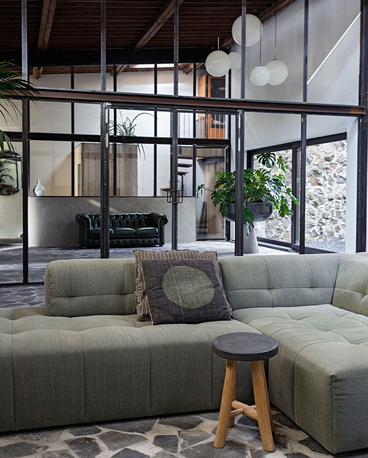Bank en kruk ByDennis, gestreept kussen vtwonen, kussen met cirkel Sissy-Boy, bollampen Meneertje Lamp, grote plantenschaal: origineel doopvont met Monstera, Chesterfield van vrienden gekocht. vtwonen 3-2022 | styling Ilona Jongepier | fotografie Dana van Leeuwen
