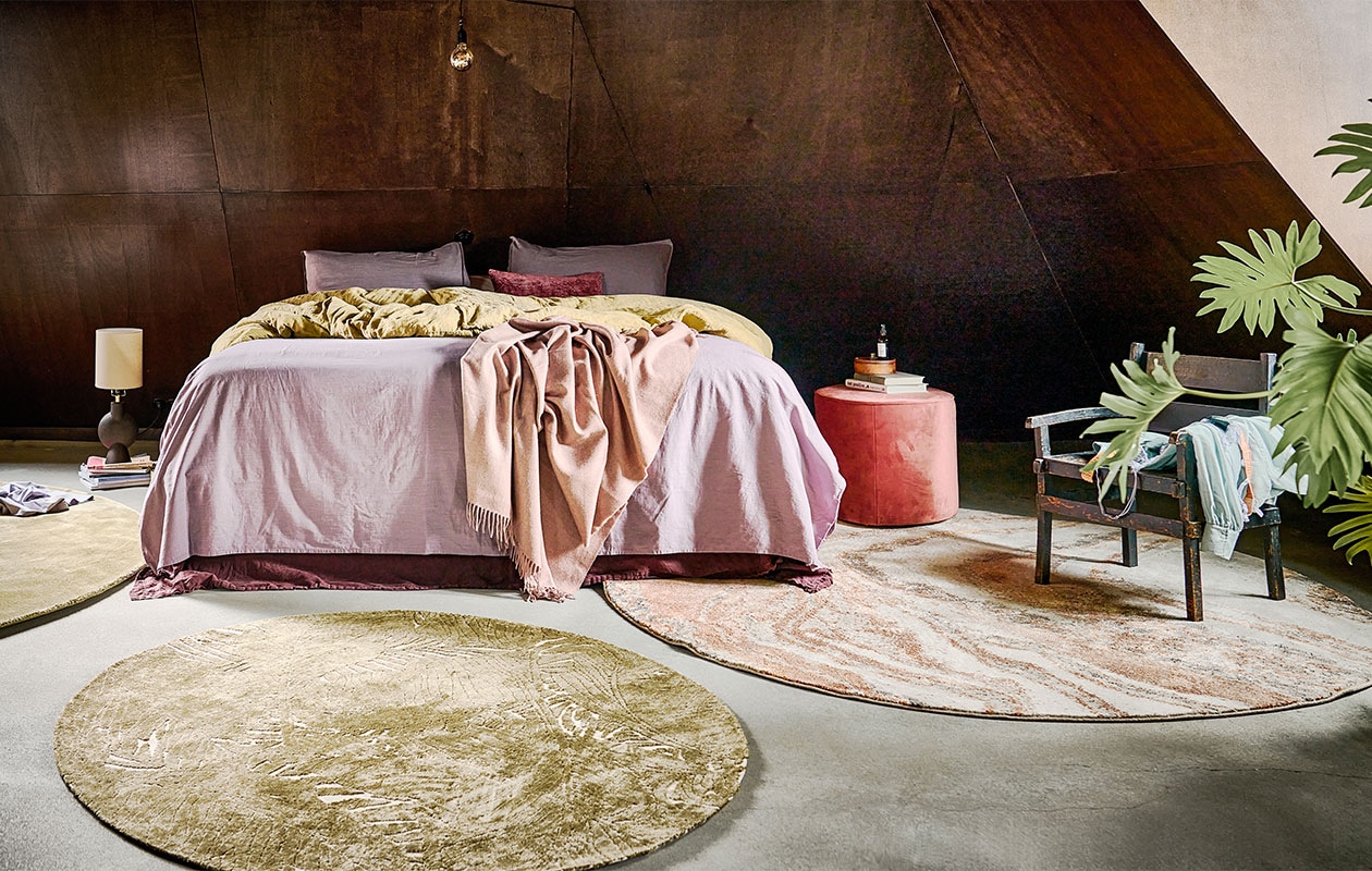 Groen vloerkleed Ravel van BePureHome, 250 cm (Ø) € 499,-, vloerkleed Naya met bladmotief van Woood, 150 cm (Ø) € 109,-, vloerkleed Solar van Zuiver 200 cm (Ø) € 339,-, tafellamp van Bloomingville € 85,-, velvet poef Sara € 69,30, lila dekbedovertrek Natural Stone van vtwonen, 240×200 cm € 97,99, dekbedovertrek Natural Stone in kleur Fraying Yellow van vtwonen, 200×200/220 cm € 92,20, plaid Cusco van Silkeborg in kleur Dusty Rose, 200×130 cm € 214,99 (vtwonen.nl). Blouse vanaf € 59,95, beha van Love Stories € 45,- (studione9en.nl). Kleine, houten doos met spiegel € 19,99 (hm.com). Kussen Soul in kleur Wine, 30×50 cm € 24,95 (basiclabel.nl). Overig privébezit. vtwonen 04-2022 | styling Marlies Does | fotografie Sjoerd Eickmans | assistentie Yara Wagner