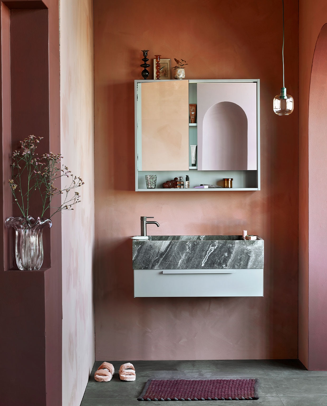 M.m.v. vestingh.nl (kleur op de muur Terra Pink No.102, kleur van kolom en rand toog Merlot Mania No. 123), zarahome.com (sloffen), vtwonen.nl (hanglamp Amp van Normann Copenhagen), hay.nl (bruine glazen opbergpot met deksel Container S, vloerkleed Burgundy, tandenborstel Tann, sculpture W&S Moguls Burgundy), nordal.eu (gekleurde glazen kandelaars, roze vaas, gespikkeld drinkglas, roze marmeren bakje), stories.com (parfum, tubes, sieraden). Overig privébezit. vtwonen 05-2022 | productie Tanja Saarberg | styling Kim van Rossenberg | fotografie Peggy Janssen