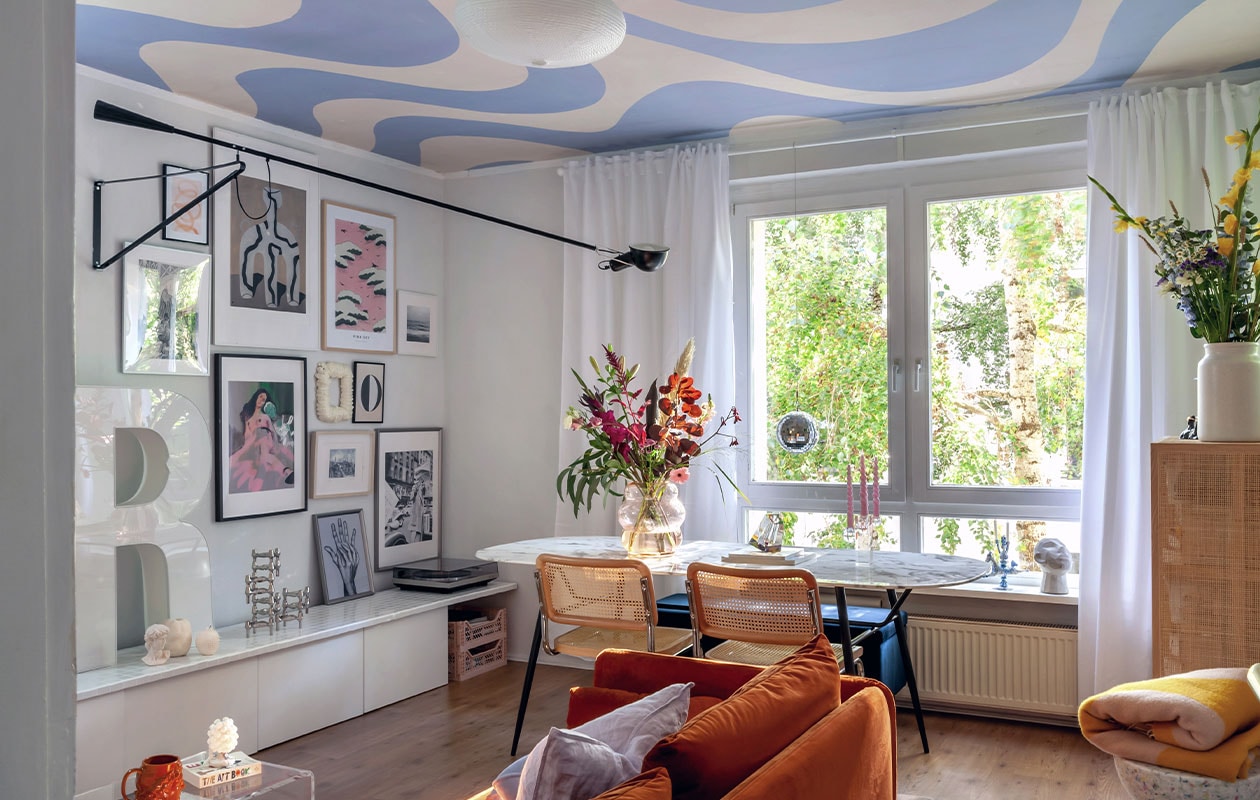 Witte lage kast (met zelf betegeld blad) en houten kast Ikea, R lichtletter via Ebay Kleinanzeigen, tafel Depot, koffietafel via Ebay, stoelen Home24, lamp Flos, beker zelfgemaakt, kruk Wild Studio, plaid Arket, glazen vaas Pols Potten, kaars Sentimental Candles. Behang op plafond Curvy van Belarte Studio. vtwonen 4-2022 | styling Agi Raw | fotografie en tekst Anne-Catherine Scoffoni | tekstbewerking Monique van der Pauw