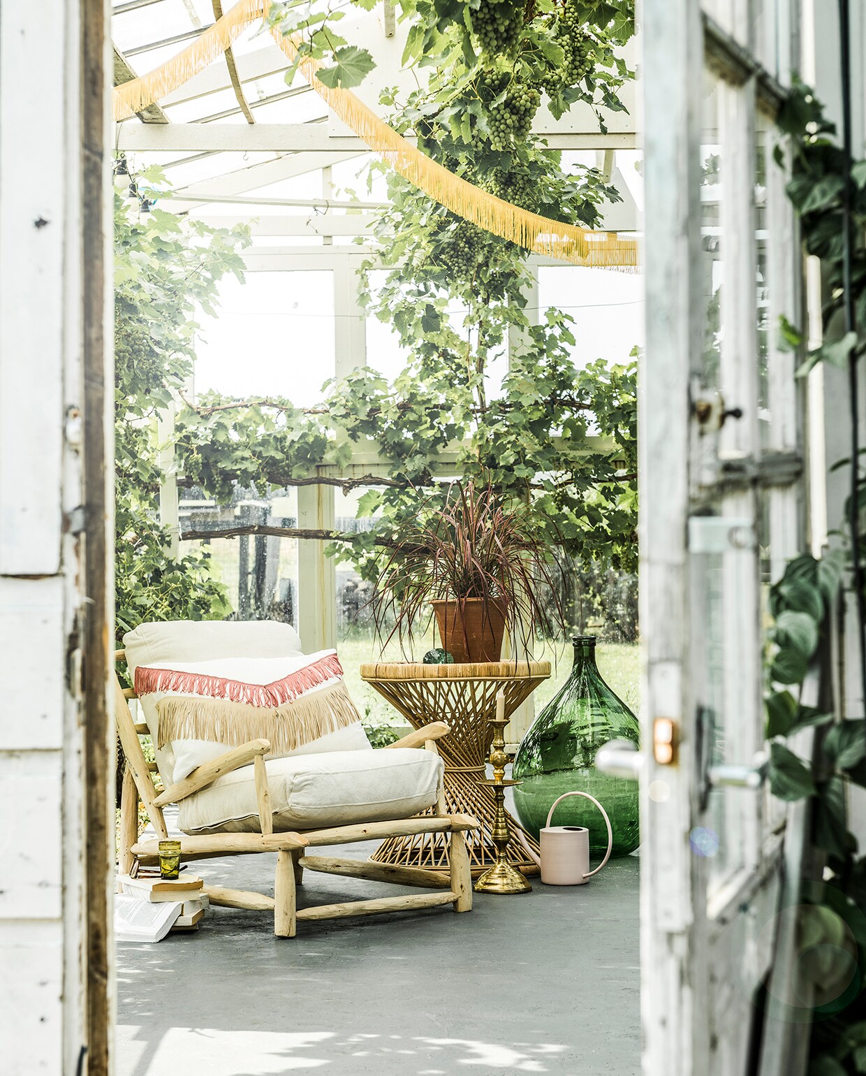 Franjeband geel en roze (aboeken.nl). Rotan bijzettafel (hkliving.nl). Kussen (ikea.nl). Groene vaas (old-basics.nl). Grote vintage koperen kandelaar , groen glas, groen glazen object (householdhardware.nl). Overig privébezit. vtwonen tuin special 2 2020 | Styling en Productie Marlies Does | Fotografie Sjoerd Eickmans | Shopping Productie Corrien Flohil