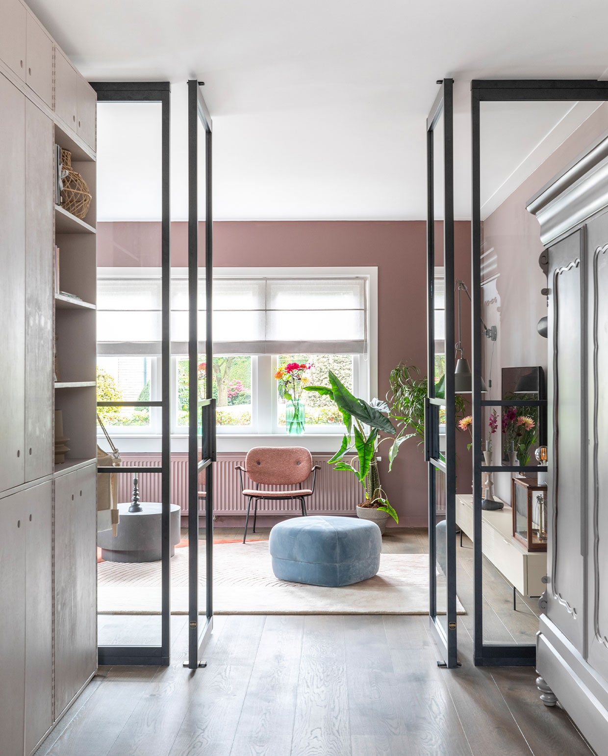 Kast links op maat gemaakt, prijs op aanvraag (com-anders.nl), geverfd met Flexa Creations lak Perky Limestone (flexa.nl). Poef van Norman Copenhagen € 660,-, vloerkleed Layered € 1290,-, fauteuil Co Lounge van Menu € 1230,-, salontafel van Woood € 249,- (eijerkamp.nl). Beige vaas van Bloomingville € 49,90, bruine vaas van Bloomingville € 49,90, rieten mand van Frutas € 49,95, kandelaar op salontafel van BePureHome € 26,95, groene vaas in vensterbank van Bloomingville € 49,90 (vtwonen.nl). Antieke kast geverfd met Flexa Creations lak Spacious Grey (flexa.nl). Stalen taatsdeuren van keuken naar woonkamer op maat gemaakt, prijs op aanvraag (gewoongers.nl). Overig privébezit. Weer verliefd op je huis 2021 Baarn | fotografie Margriet Hoekstra | styling Fietje Bruijn