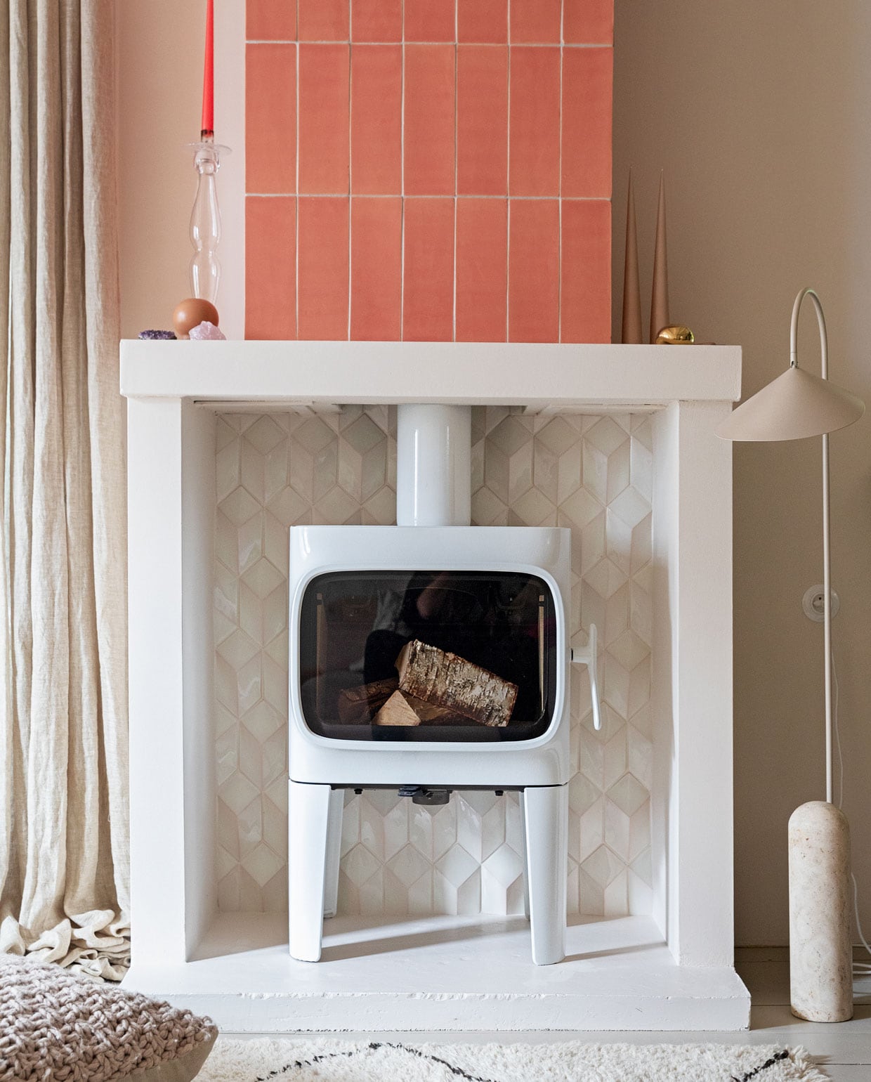 Houtkachel Jøtul F305. Tegels 10×30 cm kleur Flamingo Baby en witte tegels Constellation kleur Eggshell White via Quintalisque. Kussen Sukha. Lamp en kiezel Ferm Living. Glazen kandelaar herkomst onbekend. Kaarsen Ester &amp; Erik. vtwonen 2-2022 | Styling Ilona Jongepier | Fotografie Dana van Leeuwen