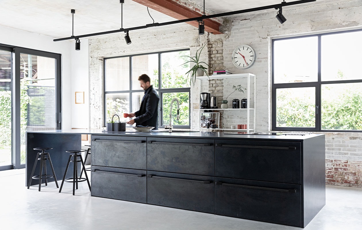 De keuken is een eigen ontwerp, binnenwerk op maat gemaakt door Marcel Hermans, beplating en werkblad van blauwstaal Schouren Metaal. Railarmatuur Venled. Toolbox Ferm Living. Krukken en open kast Ikea. Klok onbekend. Keukenblok eigen ontwerp, maatwerk, afgewerkt met geglazuurde tegels Praxis. Houten wand Okoume platen Bouwcentrum Driessen. Houten schappen koffiebar resthout meubelfabriek, deels geverfd in kleur Geordend van Histor. vtwonen 01-2022 | styling Ilona Jongepier | fotografie Dana van Leeuwen