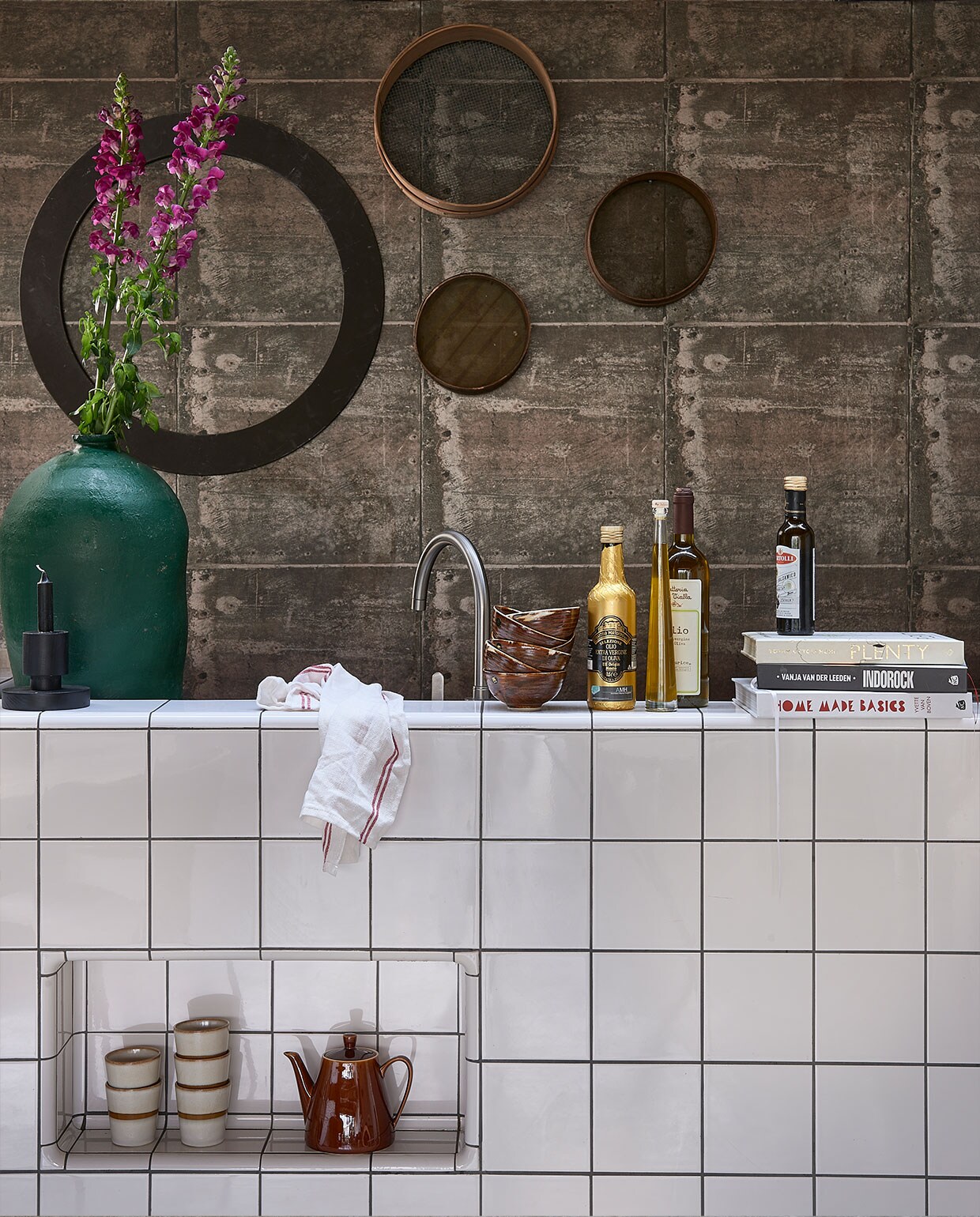 Behang met print van verweerde roestige metalen platen met klinknagels, 53 cm x 10,05 m, per rol € 49,50 (originwallcoverings.nl). Hoge groene olijfpot € 140,-, zeven aan de wand vanaf € 15,- (vandijkenko.nl). Bruine dessertschaaltjes, per stuk € 7,50, mok € 8,50 (hkliving.nl). Glazendoek € 0,39 (ikea.nl). Kandelaar zwart € 27,95 (fonq.nl). Koffiepot privébezit. vtwonen 3-2022 | Styling Fietje Bruijn | Fotografie Dennis Brandsma\n