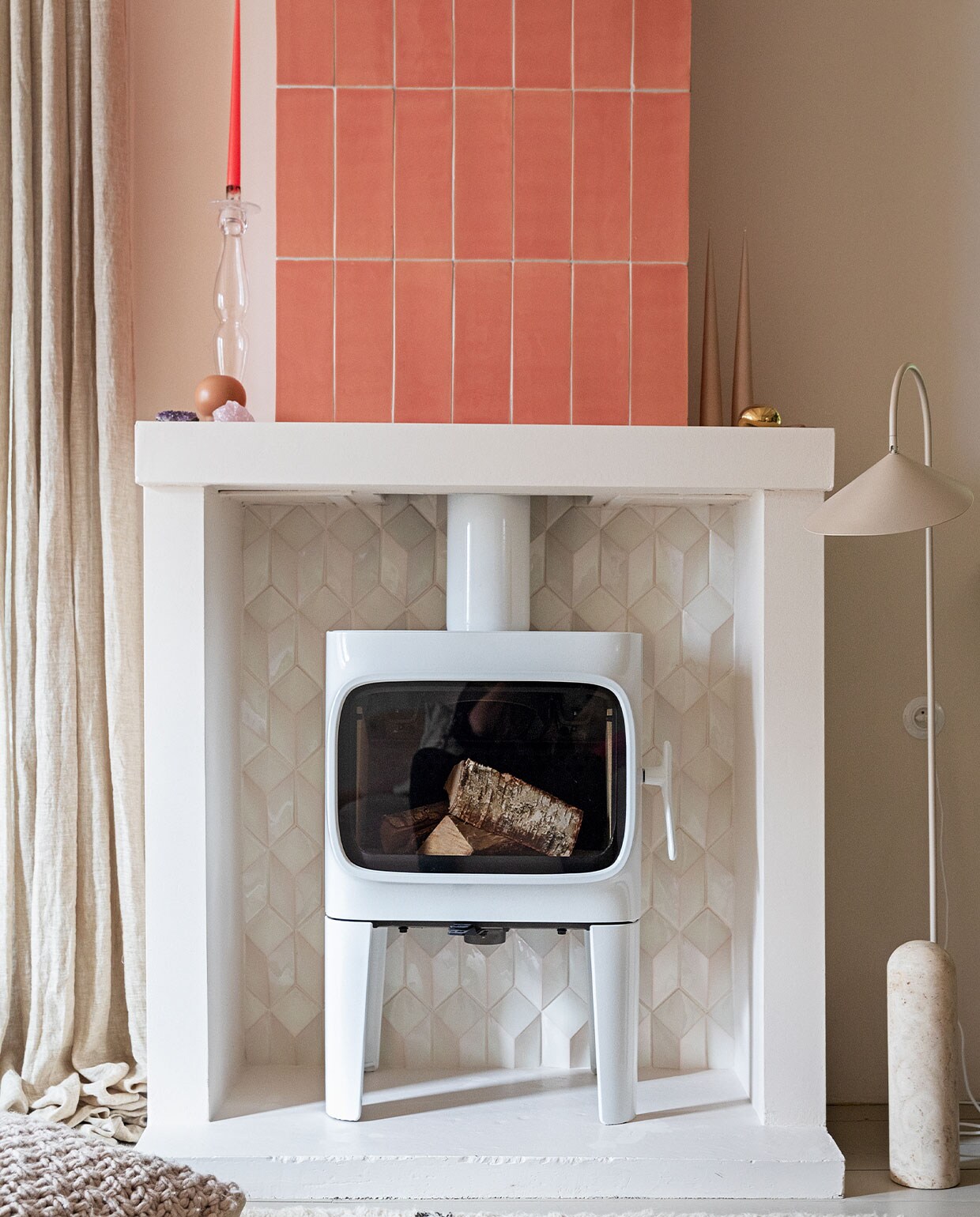 Houtkachel Jøtul F305. Tegels 10×30 cm kleur Flamingo Baby en witte tegels Constellation kleur Eggshell White via Quintalisque. Kussen Sukha. Lamp en kiezel Ferm Living. Glazen kandelaar herkomst onbekend. Kaarsen Ester &amp; Erik. vtwonen 2-2022 | styling Ilona Jongepier | fotografie Dana van Leeuwen | tekst Martine de Hoog
