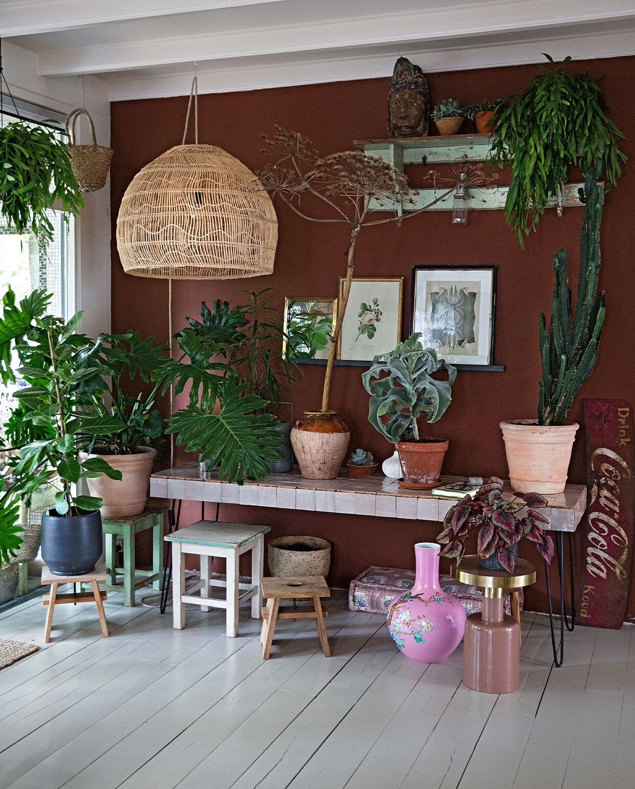 Tafel zelfgemaakt (tegels Household Hardware en hairpin-poten bol.com). Rieten lamp HKliving. Coca Cola bord op straat gevonden. Bijzettafel met gouden blad Zuiver. Roze vaas van Pols Potten via Wim van Assem bloembinderij. Kussen en spiegel Household Hardware. Prullenbak cadeau gekregen. Melkkruk eigen ontwerp Isi i.s.m. Geralt Ploegstra. Krukken achter Loods 5. Zwarte bloempot vtwonen. Olijfpot cadeau gekregen. Pot rechts en terra pot Ranzijn. Boeddha hoofd, schilderij midden en kapstok brocante markt. Schilderij rechts Hanneke van de Pol via Artwall Collection. Manden met hangplanten meegenomen uit Ibiza. vtwonen 2-2022 | styling Ilona Jongepier | fotografie Dana van Leeuwen | tekst Martine de Hoog