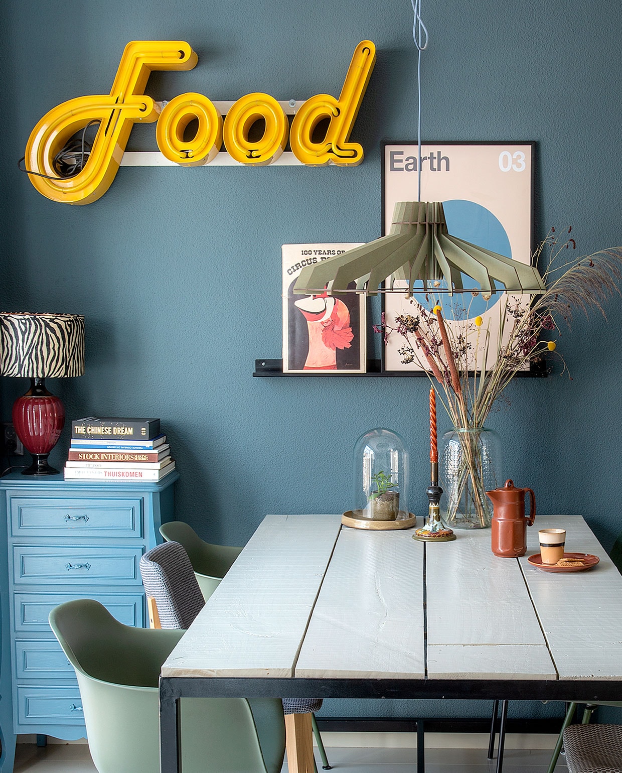Wandkleur Vintage blauw van Karwei. Vintage neon gekocht van een bevriende leverancier. Tafel zelf gemaakt, kuipstoelen Karwei, grijze stoel Joe van Midj. Hanglamp Van Tjalle &amp; Jasper. Lampenkap Kwantum, vaas Leen Bakker. Poster Earth van Desenio, ernaast een oud circusboek. Stolp, bord Mica Decorations. Beker HKliving. Kast, lampvoet, koffiekan, kandelaar van de kringloop. Stalen schilderijrichel gemaakt door Bas en collega. vtwonen DIY special 4 | Fotografie Ton Bouwer | Productie Monique van der Pauw