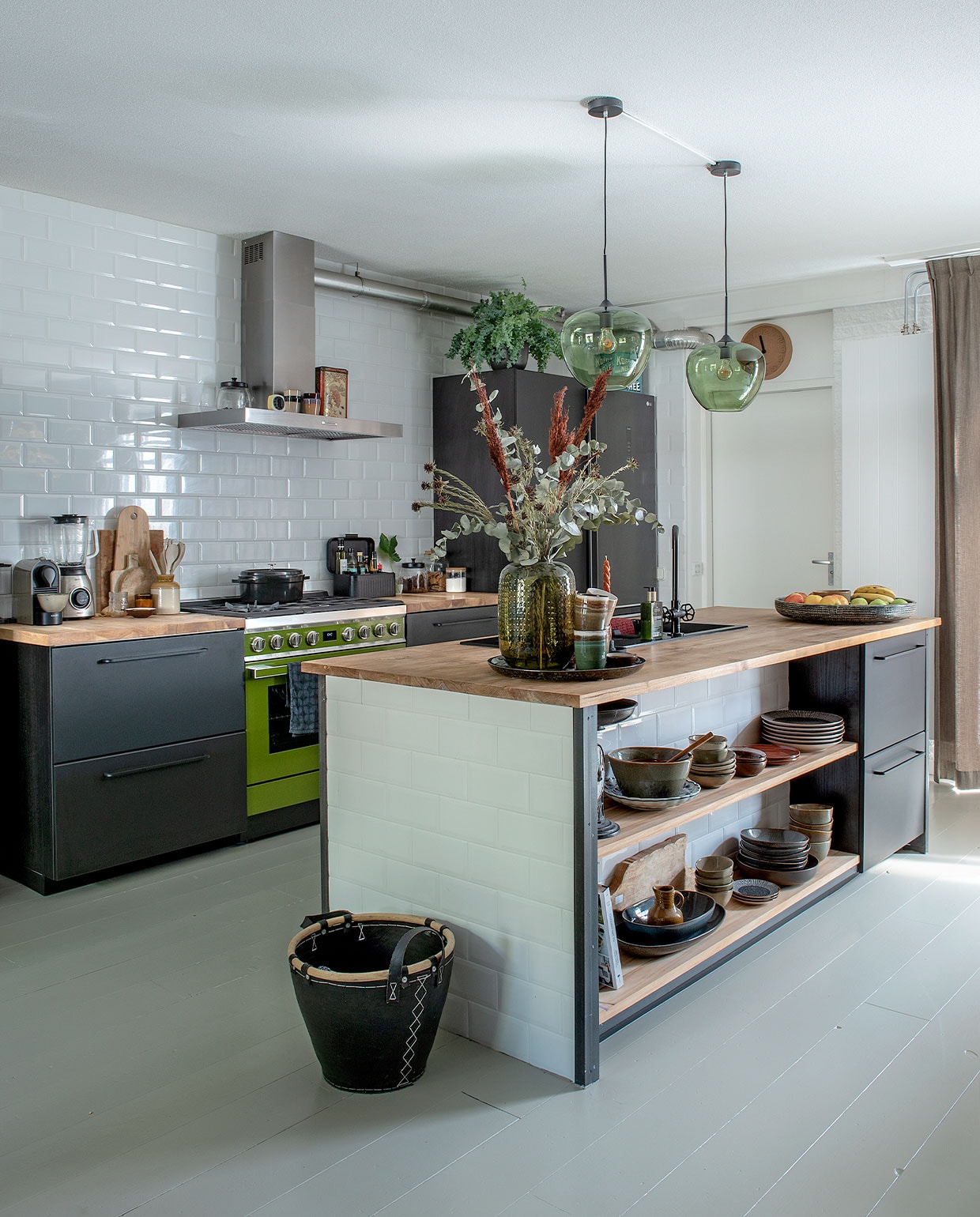 Keukenkasten Kungsbacka, wasbak en kraan van Ikea. Teakhouten werkbladen op maat gemaakt. Fornuis Smeg. Metrotegels Praxis. Hanglampen Light &amp; Living. Pan Albert Heijn, blender Philips, koffieapparaat Krupps. Koffer Kwantum, vaas Intratuin, klok Zuiver. Theedoek Hema. Servies Xenos, Mica Decorations, Kitchen Trend, Kwantum. Mand van oude fietsbanden Leen Bakker. Verf vloerdelen Rijksmuseum groen van Sikkens. vtwonen DIY special 4 | Fotografie Ton Bouwer | Productie Monique van der Pauw