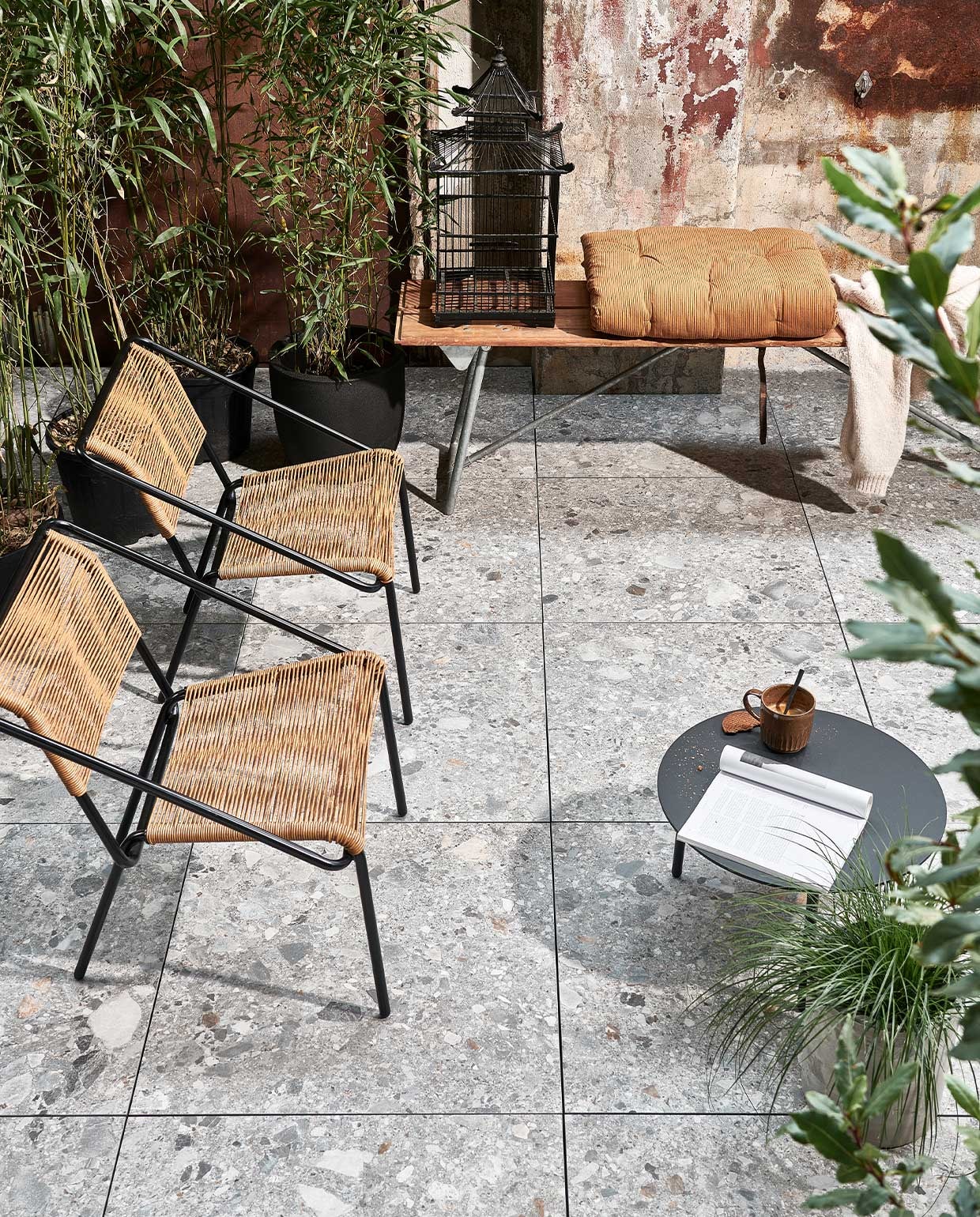 Buitentegels Solostone Uni Composite mix, 70x70x3,2 cm per m² € 69,95. M.m.v. basiclabel.nl (fauteuils Wisp van BePureHome), com-anders.nl (bank, vogelkooi), vtwonen.nl (bijzettafel van Serax, beker, grijze betonlook bloempot), deens.nl (terrakleurige matras van Madam Stoltz). vtwonen 04-2022 | productie Tanja Saarberg | styling Marlies Does | dotografie Sjoerd Eickmans