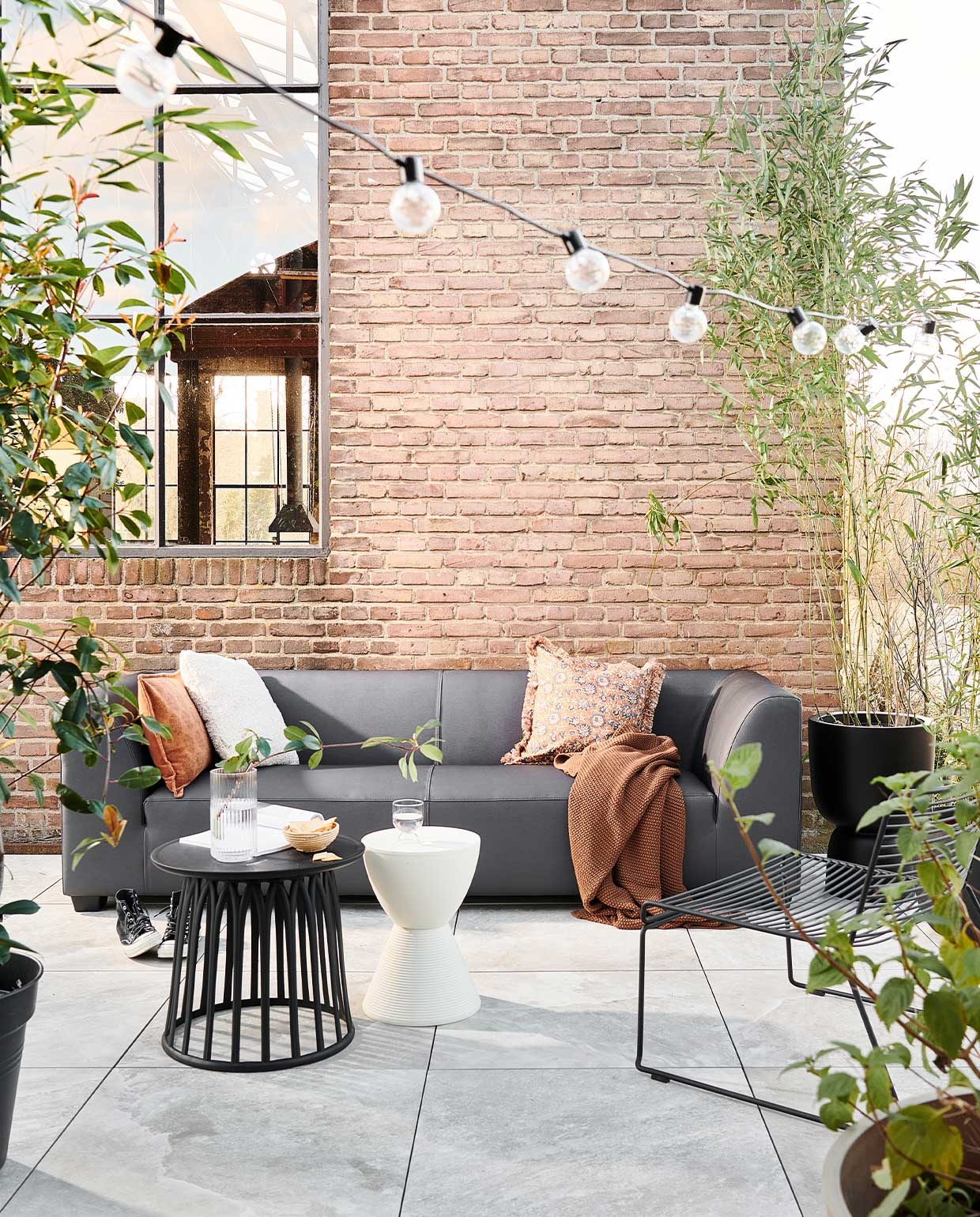 Buitentegels Solostone Uni Clouds 70x70x3,2 cm per m² € 69,95.3-zits buitenbank Hollandia van vtwonen € 1099,-, verkrijgbaar via basiclabel.nl, vtwonen.nl. M.m.v. vtwonen.nl (kruk van Kartell, deken van Marc O’Polo, kussen van Bloomingville, lichtsnoer, hoge pot op voet van Elho, lage zwarte pot van Capi), basiclabel.nl (zwarte kunststof bijzettafel), com-anders (mand), vandijkenko.nl (stoel). vtwonen 04-2022 | Productie Tanja saarberg | Styling Marlies Does | Fotografie sjoerd eickmans
