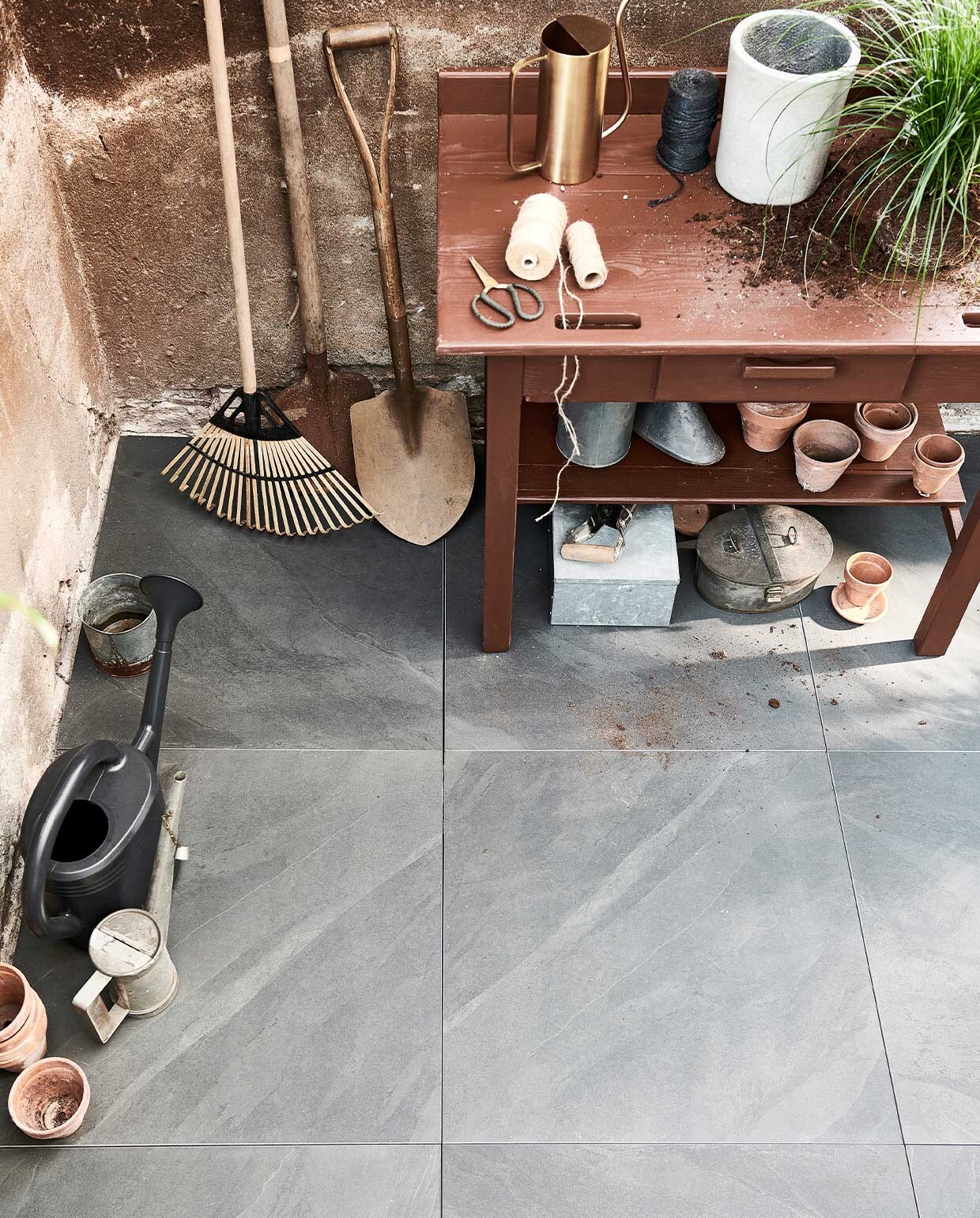 Buitentegels Solostone Uni Waves Antracite, 70x70x3,2 cm per m² € 69,95. M.m.v. vtwonen.nl (klapkruk met stoffen zitting van Ferm Living, zwarte gieter van Elho), com-anders.nl (scheppen, houten tafel, oud zink, mand met strepen), intratuin.nl (terracotta potten, hark van hout en bamboe, snoeischaar). vtwonen 04-2022 | Productie Tanja saarberg | Styling Marlies Does | Fotografie sjoerd eickmans\n