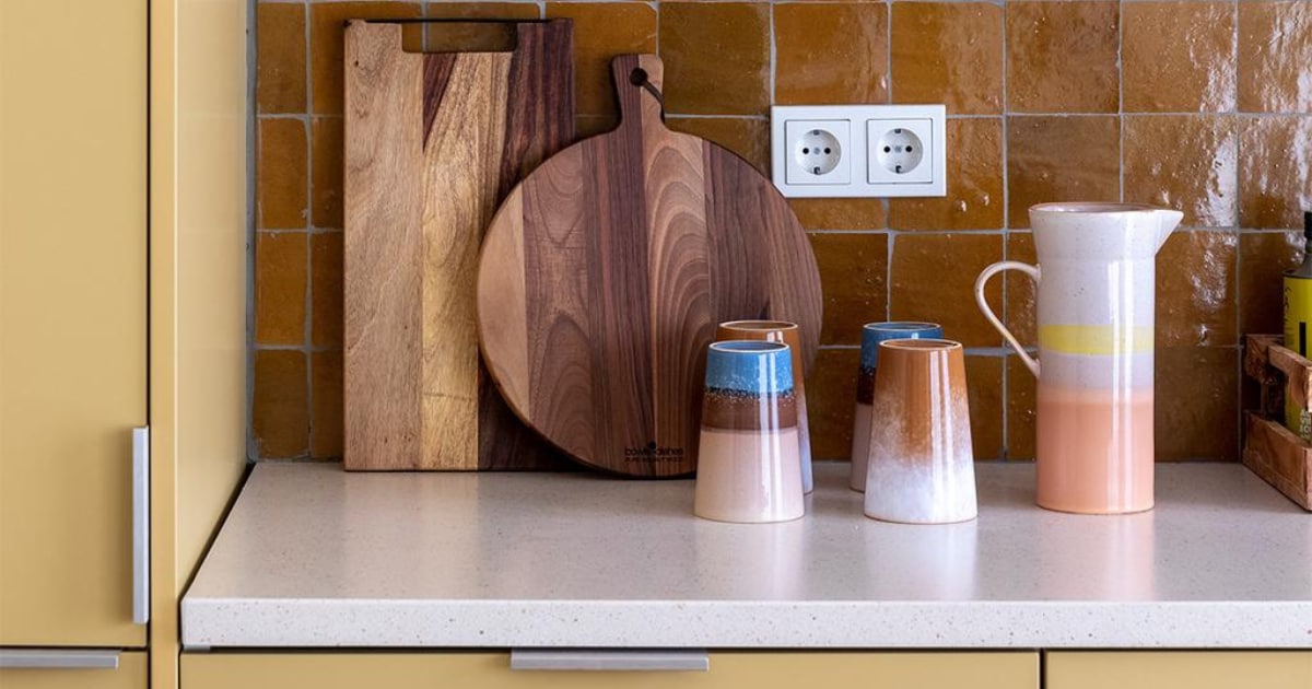 Flexa Creations muurverf om raam Midden Zandstrand (flexa.nl). Keukenkastfronten op maat gemaakt, prijs op aanvraag (k14.nl). Tegels achterwand Zelliges Mustard, per m² € 114,95 (householdhardware.nl). Houten planken van Bowls en Dishes vanaf € 15,-, koraalkleurige kandelaar van À la € 30,-, gele kandelaar Flare van Hay € 49,-, groene glazen vaas van Bloomingville € 38,90 (vtwonen.nl). Vijzel € 28,44 (bowls-dishes.nl). Kan € 29,95 en theemokken € 11,40 van HKliving (eijerkamp.nl). Kunstwerk Neutrale collage van Laura Horn € 50,- (werkaandemuur.nl). JA | vtwonen weer verliefd op je huis extra seizoen 15, aflevering 3 | styling Marianne Luning | fotografie Margriet Hoekstra