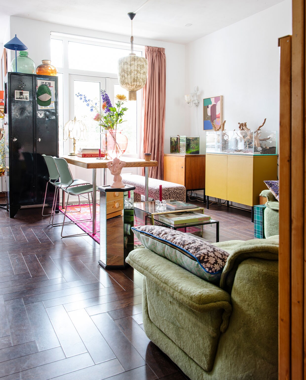 Groene fluwelen bank @vanvintagetayko. Kussens, roze tapijt en bankje Doris voor HKliving. Eettafel Marktplaats. Stoelen Krueger Matrix. Roze vaas Rataplan. Alle kandelaars cadeau gekregen. Vierkante koffietafel Noppes, zeshoekige koffietafel De zaak van Sjaak. Roze beeld en lamp aan de muur Fortune Flea. Zwarte kast gekregen. Groene vaas Van Dijk &amp; Ko, vazen op de kast Vok Jong Bloemen en Planten. Hanglamp Vintage Depot. Gordijnen Noordermarkt. Schilderij HKliving. Lage kast tegen de muur links gevonden langs de weg met klein aquarium van Rainer. Kast rechts met terrarium gemaakt door Mark en z’n opa. Vloer zat al in het huis. vtwonen 2-2022 | Productie Insidehomepage | Styling Kim Timmerman | Fotografie Louis Lemaire | Tekst Inge van Lieshout | Tekstbewerking Merel van der Lande