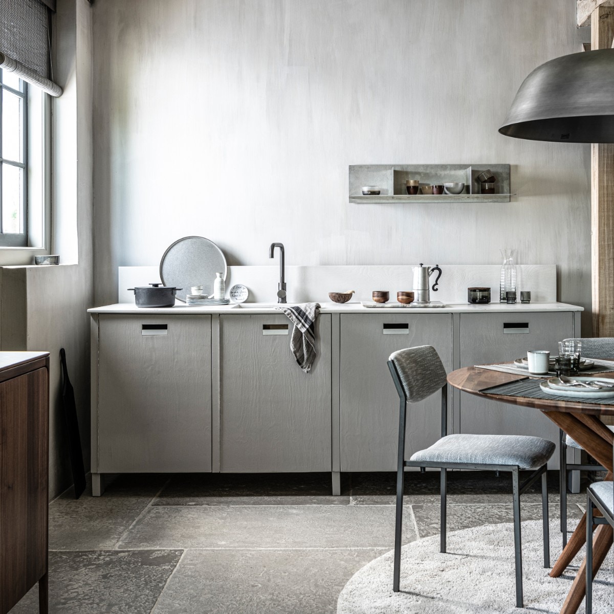 Op de wanden kalkverf Warm Grey van Pure &amp; Original 1 liter € 40,75 (pure-original.nl).Keuken op maat gemaakt, prijs op aanvraag (com-anders.nl). Kraan gun metal € 169,- (tworooms.nl). Zwarte pan Surface van Serax € 126,-, glas Ripple van Ferm Living, set van 4 € 35,-, zwarte serveerplank Acacia van Bloomingville 70 cm € 60,99, houten theekop Collage van Serax, per stuk € 12,80 (vtwonen.nl). Percolator Lady Anne € 59,-, tweekleurige keramieken mok Earth € 17,50, stonewashed rond stalen dienblad € 69,- (bymolle.com). Sake set € 39,75 (japansewinkeltje.nl). Bordje met geschreven tekst van Anouk Kramer € 30,- (archive-store.nl). Glazen opbergpot met houten deksel € 19,95, glazen karaf € 24,95 (nordal.eu). Wandplank Rivet, small, onbehandeld aluminium 87,6×24,4×20,6 cm (lxdxh) € 615,- (framacph.com). Hanglamp Cloche Three, geborsteld aluminium, 81×25 cm (Øxh) € 750,- (vanduivenboden.nl). Vintage design stoelen met nieuwe stoffering € 850,-, walnoothouten eettafel Lakri 120 cm (Ø) € 2984,- (goeds.nl). Gehamerd bestek, per stuk € 5,99, bamboe placemat, set van 2 € 6,99 (zarahome.com). Ronde borden van HK Living vanaf € 11,95, rechthoekige borden van Serax vanaf € 11,95, mok van HK Living € 6,95, schaal € 10,95 (loftloft.nl). Walnoothouten dressoir Rikke € 2960,- (demachinekamer.nl). Rond grijs vloerkleed € 3034,- (homestede.nl). Roll-up gordijn bamboo flat sticks prijs op aanvraag (nature-deco.com). vtwonen 11-2021 | styling Kim van Rossenberg | fotografie Sjoerd Eickmans | assistentie Sanne van der Beek en Meike Linthorst
