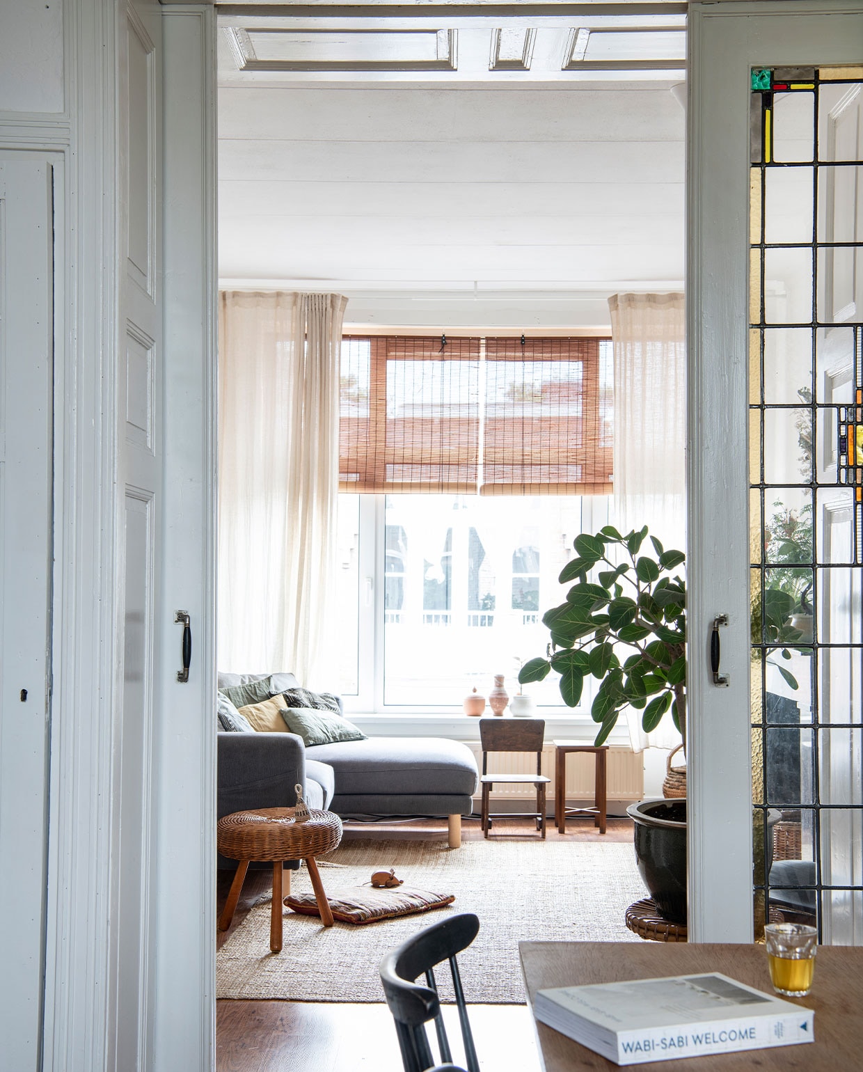 Stoelen en krukken tweedehands. Bank en kleed Ikea, gordijnen H&amp;M Home, rolgordijnen bol.com. Grote plantenpot tweedehands, plant Ficus benghalensis. Overig herkomst onbekend. vtwonen 02-2022 | productie Insidehomepage | styling Inge van Lieshout | fotografie Louis Lemaire