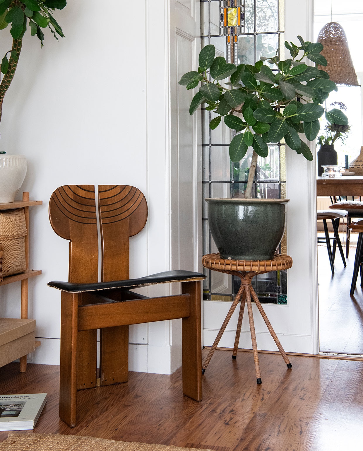 Stoel vintage, rotan tafel en grote pot tweedehands, kleed Ikea, planten Euphorbia Madagascar Jewel, Ficus benghalensis. Tafel en gevlochten mand tweedehands, Farstrup-spijlenstoelen Hit &amp; Run. Lamp zelfgemaakt van visnet, zwarte vaas D&amp;M Deco, kandelaar Rustik Lys. vtwonen 02-2022 | productie Insidehomepage | styling Inge van Lieshout | fotografie Louis Lemaire