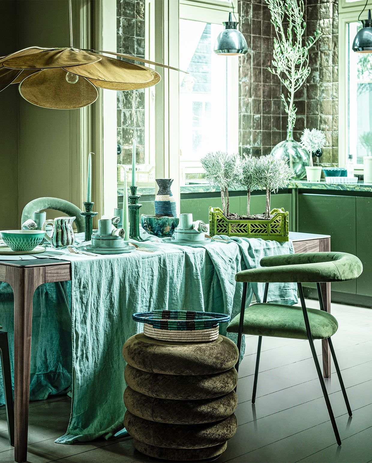 Tafel Rikke walnoot met Fenix blad, 160x90x76 cm (demachinekamer.nl). Poef (fermliving.com). Velours stoel links Gubi Beetle, glazen fles op trolley (homestede.nl). Velours stoel rechtsachter (covanderhorst.nl). Houten stoel Bliss van Woood, velours stoel rechtsvoor Haily van Dutchbone, trolley Mil van Dutchbone, rond bord Surface van Serax, per 4, ovaal tapasbord Surface van Serax, braadpan Surface van Serax, water­glazen Raami van Iitala, per 2, goudkleurig bestek Amefa vintage 24-delig, taartvorm tarte tatin van Jamie Oliver (vtwonen.nl). Wijnglas op trolley (zarahome.com). Waterflessen, krat klein prijs op aanvraag, krat groot, kan gestreept, kandelaars en kaarsen prijs op aanvraag, opgestapeld: kopjes klein, per stuk, borden, schaaltjes middel, per stuk, groenblauwe gevlekte schaal, voorraadpot prijs op aanvraag, groene schaal op keukenblad (loods5.nl). Linnen tafellaken, 320×270 cm, mand, hoge kan (couleurlocale.eu). Koffertje, lamp, Ø 120 cm (archive-store.nl). Kussen (hinck.nl). Linnen servetten, per 2 (hm.com). Grote vaas (oudebouwmaterialen.nl). Groene schaal op tafel (ottomania.nl). Placemat (bijenkorf.nl). Plantenpot (uncwardrobe.com). Schilderij Branch on a green canvas, 80×100 cm (maartjevandennoort.nl). vtwonen 04-2020 | styling Liza Wassenaar | fotografie Sjoerd Eickmans