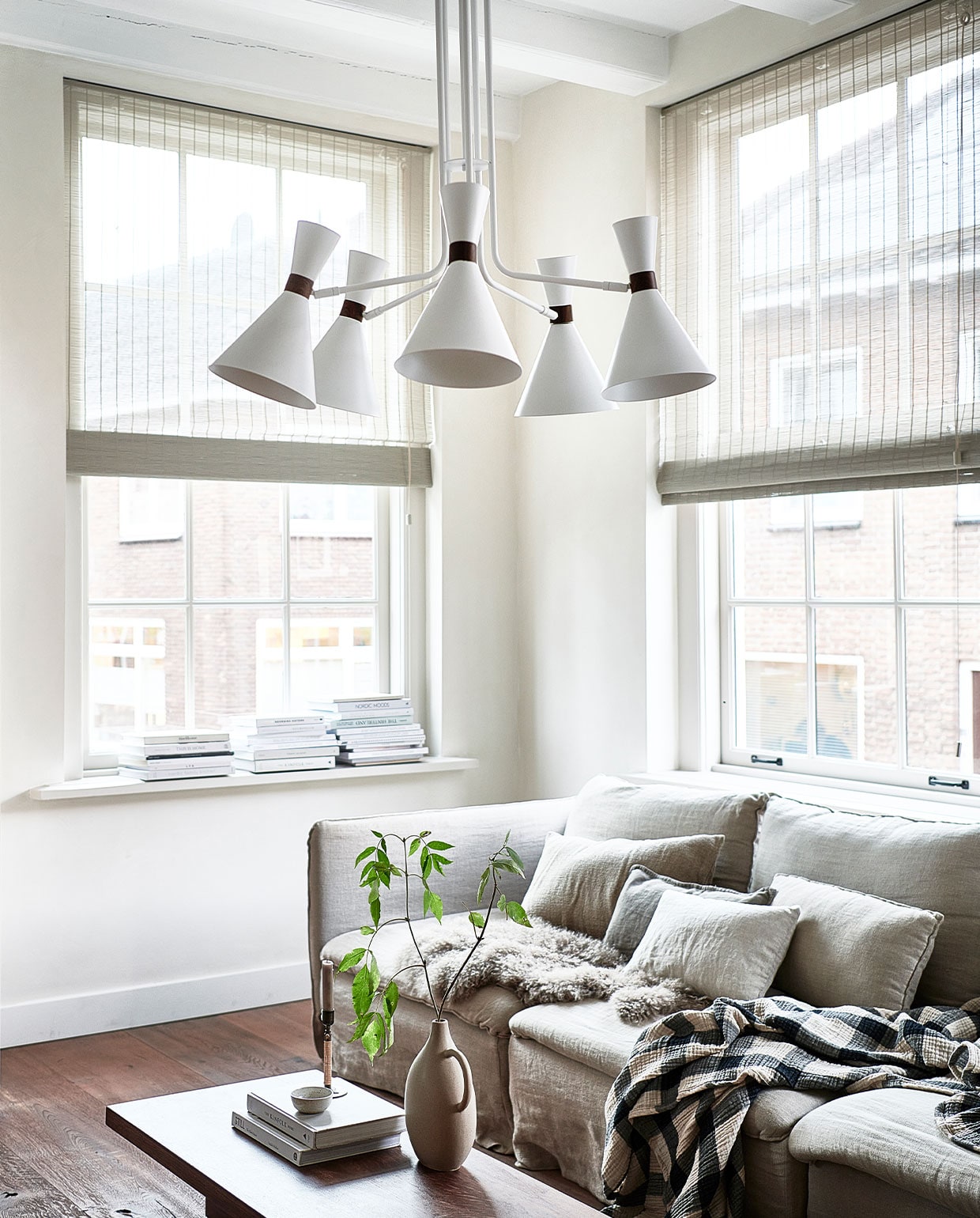 Matte zandgrijze metalen hanglamp Hoodies (5 lampen), 20x86x83,5 cm (ook verkrijgbaar in matzwart). M.m.v. ikea.nl (bank Söderhamn), bemz.com (linnen hoes voor de bank), zarahome.com (vaas, kussens), hm.com (geblokt plaid), karwei.nl (schapenvacht), bauwerkcolour.com (muurverf kleur Mykonos), nature-deco.com (raamdecoratie). Overig privébezit. vtwonen 3-2022 | productie Tanja Saarberg | styling Kim van Rossenberg  | fotografie Sjoerd Eickmans