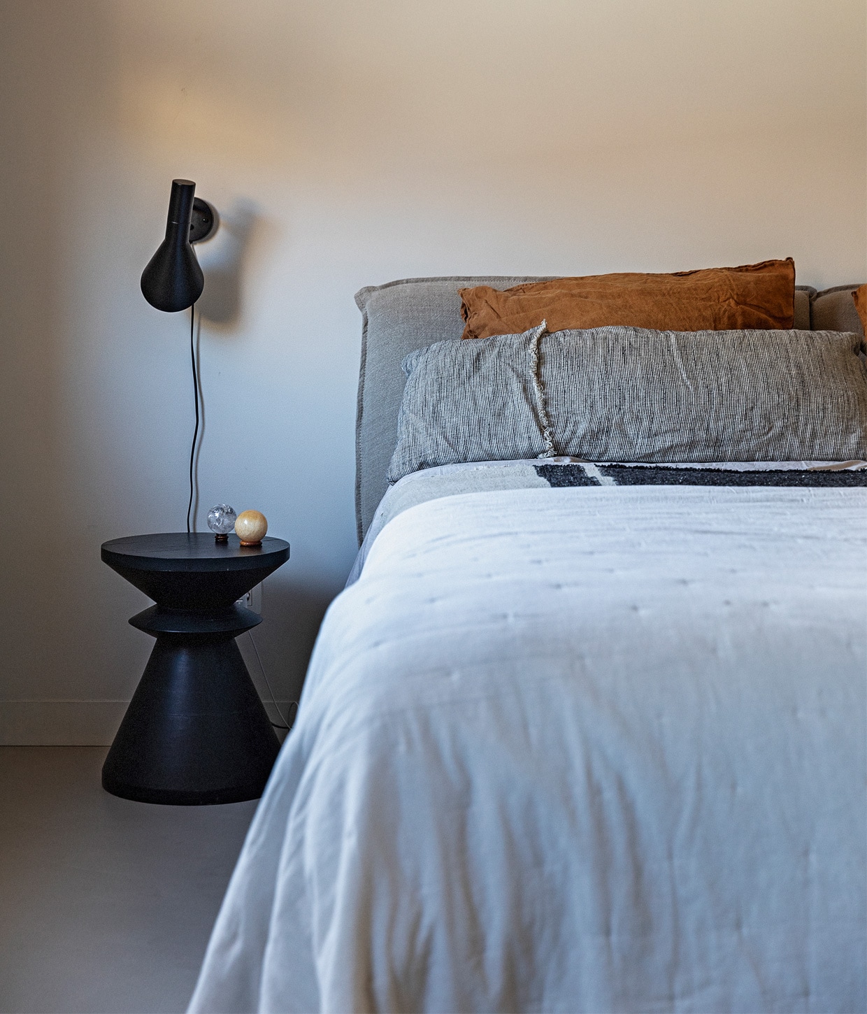 Muurverf Papyrus van Gamma, bed en bijzettafel La Redoute. Wandlamp AJ vanLouis Poulsen, item op bijzettafel erfstuk van Ediths vader. Wit, lichtgrijs enkaneelkleurig beddengoed H&amp;M Home, grijs beddengoed Zara Home, grijsblauwbeddengoed met streep The Recollection. vtwonen 13-2020 | Styling Ilona Jongepier | Fotografie Dana van Leeuwen | Tekst Anna van der Heijden