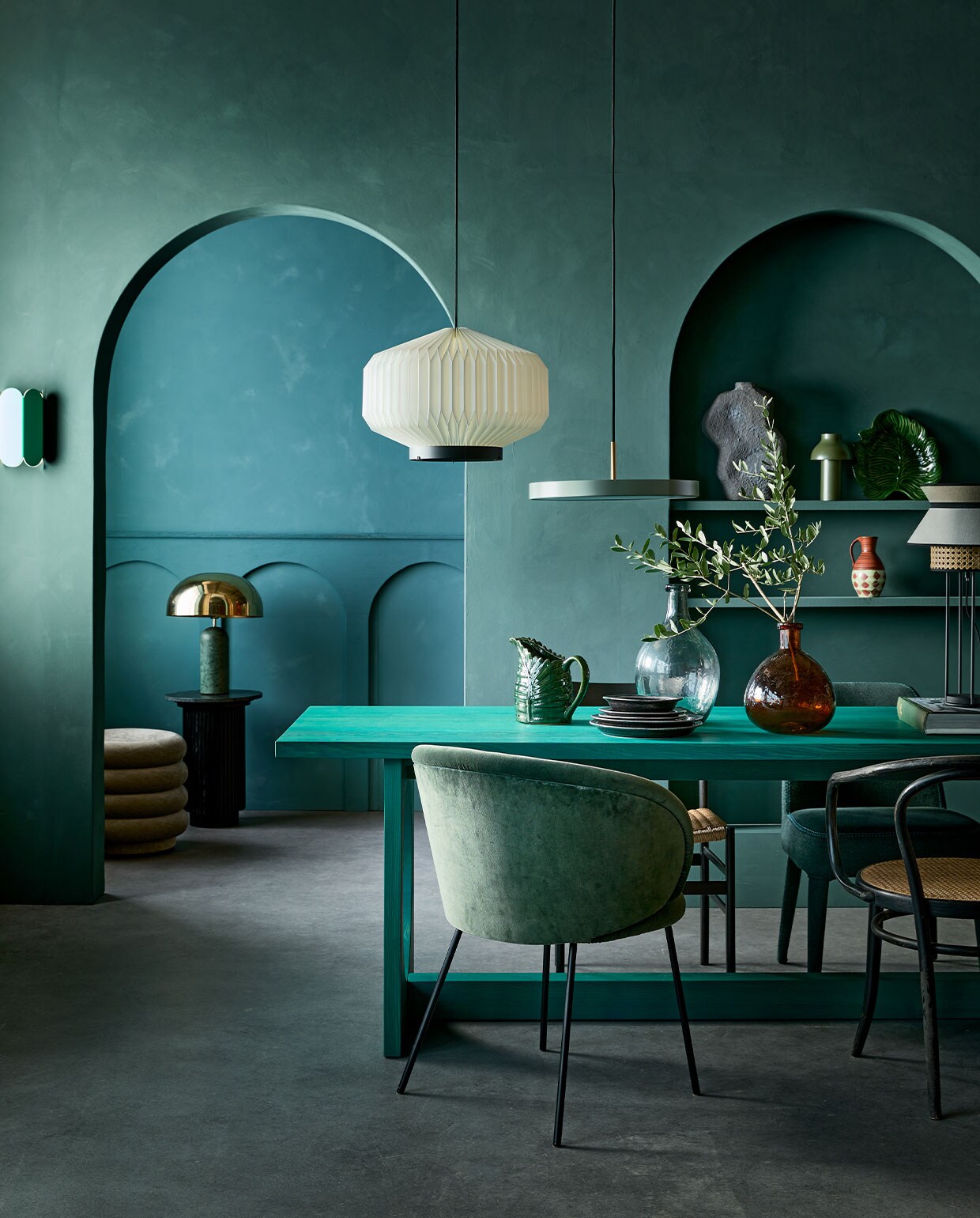 Kalkverf op de achterste muur 87 Petrol, op de muur met bogen Staal/Steel 97, 2,5 liter € 126,- (lauthentique.nl). Witte geplisseerde hanglamp Lamella Gold, 35 cm (Ø) € 838,- (leklint.dk). Groene metalen hanglamp Asteria van Umage € 289,-, groene tafellamp PC Portable van Hay op plank € 89,10, groene wandlamp Arcs van Hay € 215,- (vtwonen.nl). Poef Faded Velvet van Ferm Living € 695,-, eetkamerstoel Ona vanaf € 968,-, eetkamerstoel Febo vanaf € 1177,- (edha-interieur.nl). Tafellamp met marmeren voet en gouden kap € 435,-, marmeren bijzettafel € 419,89 (nordal.eu). Groene kan met bladvorm € 35,-, schaal met bladpatroon € 37,50 (maisonnl.com). Vintage vaasje in kast € 15,- (vandijkenko.nl). Grijze sculpturale vaas links op plank vanaf € 79,- (lanena-home.com). Zwarte eetkamerstoel met cord zitting, per 4 € 1000,- (vintagehoarder.com). Zwarte dinerborden, per stuk € 21,90, kleine zwarte borden, per stuk € 18,90, groene flesvaas € 37,25, bruine flesvaas € 33,95 (iblaursen.nl). Tafellamp Singapour van Market Set met webbing en kap € 293,- (fonq.nl). Eettafel Loop van Sarah Trenité for design label Bowden Cable, exclusief verkrijgbaar bij Friday Next Studio, prijs op aanvraag (fridaynext.nl). Overig privébezit. vtwonen 1-2022 | styling Cleo Scheulderman | fotografie Jeroen van der Spek | decorbouw Milo Kol