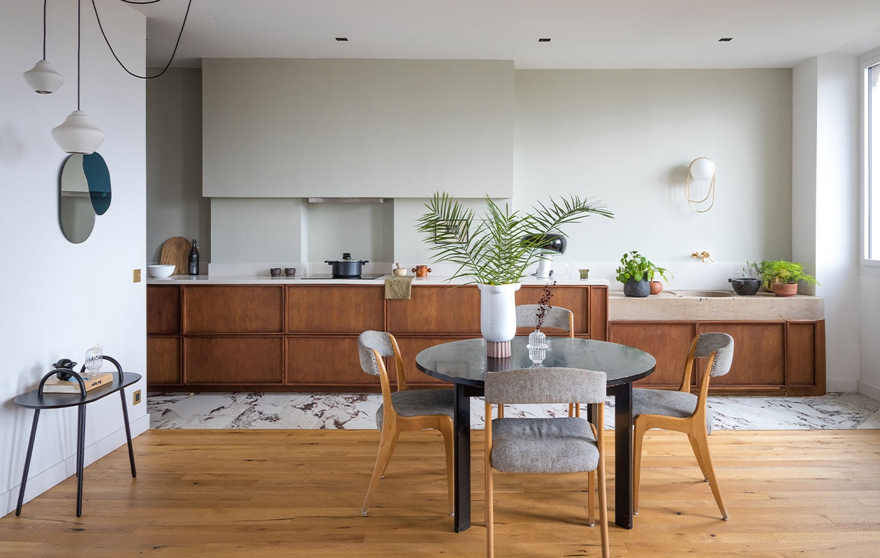 Eiken keuken uitgevoerd door timmerman, Corian werkblad. Stenen vloer Marbre van Marazzi. Vintage tafel Habitat, stoelen vlooienmarkt. Bijzettafel, wandlamp, grote vaas Oli, spiegel Maré, hanglamp voor Cfoc Paris en geurkaars Margaux Keller. Muurverf Cromarty van Farrow &amp; Ball. Overig onbekend. vtwonen 01-2022 | Productie en tekst AC Scoffoni | Styling Marie-Maud Levron | Fotografie Cécile Perrinet-Lhermitte