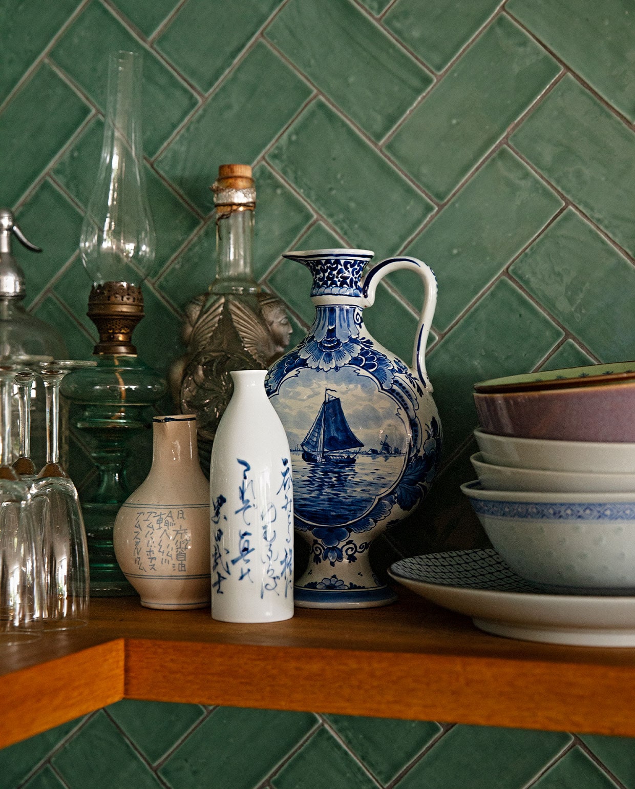 Handgevormde donkergroene tegels Metrotegel, champagneglazen gekregen, olielamp, vaasje, karaf, hoge fles erfstuk, set decoratie overblijfsel van een fotoshoot, borden en kommetjes verzameling van Aziatische winkels in New York en Amsterdam. vtwonen 09-2021 | fotografie Dana van Leeuwen | styling Ilona Jongepier