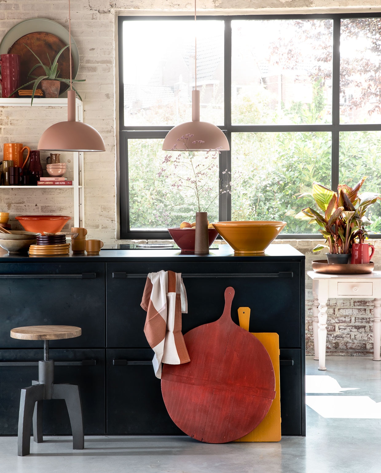 Zachtroze hanglampen Dome Shade van Ferm Living inclusief roze fitting high per stuk € 269,- (vtwonen.nl). Draaikruk Space van BepureHome € 99,- (Woondock). Grote oude kaasplanken per stuk € 35,- (H&amp;M Home), gelakt met Perfection zijdeglans lak in dieprood en mosterdgeel, 750 ml € 25,99 (Histor). Theedoek € 4,99, okergele kopjes per stuk € 5,99, okergele borden per stuk € 7,99, donkerpaarse borden per stuk € 4,99 (H&amp;M Home). Okergele schaal € 35,-, donkerrode schaal € 25,- (In-Petto). Beige schalen per stuk € 12,49 (Intratuin). Bovenop de kast: grote donkerrode kan € 35,- (In-Petto), theedoeken in okergeel en donkerpaars per stuk € 4,99 (H&amp;M Home), koper­kleurige schaal van BePureHome € 39,95, zachtgroene schaal € 24,95 (Woondock). Midden in de kast: zachtroze schaaltjes per stuk € 7,50, okergele kan € 35,- (In-Petto). Donkerpaarse kopjes per stuk € 5,99 (H&amp;M Home). Donkerrode karaf Nikki € 21,99, lichtbruine karaf € 8,99 (Intratuin). Beige kan € 8,99 (Intratuin). Onder in de kast: terracotta schaal € 35,-, okergele diepe borden € 12,50 (In-petto). Zachtroze tafeltje € 175,- (Combitex). Koperkleurige schaal Big Waitress van BePureHome € 24,95 (Woondock). Donkerrode kleine kan € 25,- (In-Petto). Kamerplanten Canna Hybride per stuk € 9,99 (Intratuin). De keuken is een eigen ontwerp van de bewoners, binnenwerk van hout, blad en kasten afgewerkt met blauw staal. Overig privébezit. vtwonen 11-2018 | styling Moniek Visser | fotografie Peggy Janssen