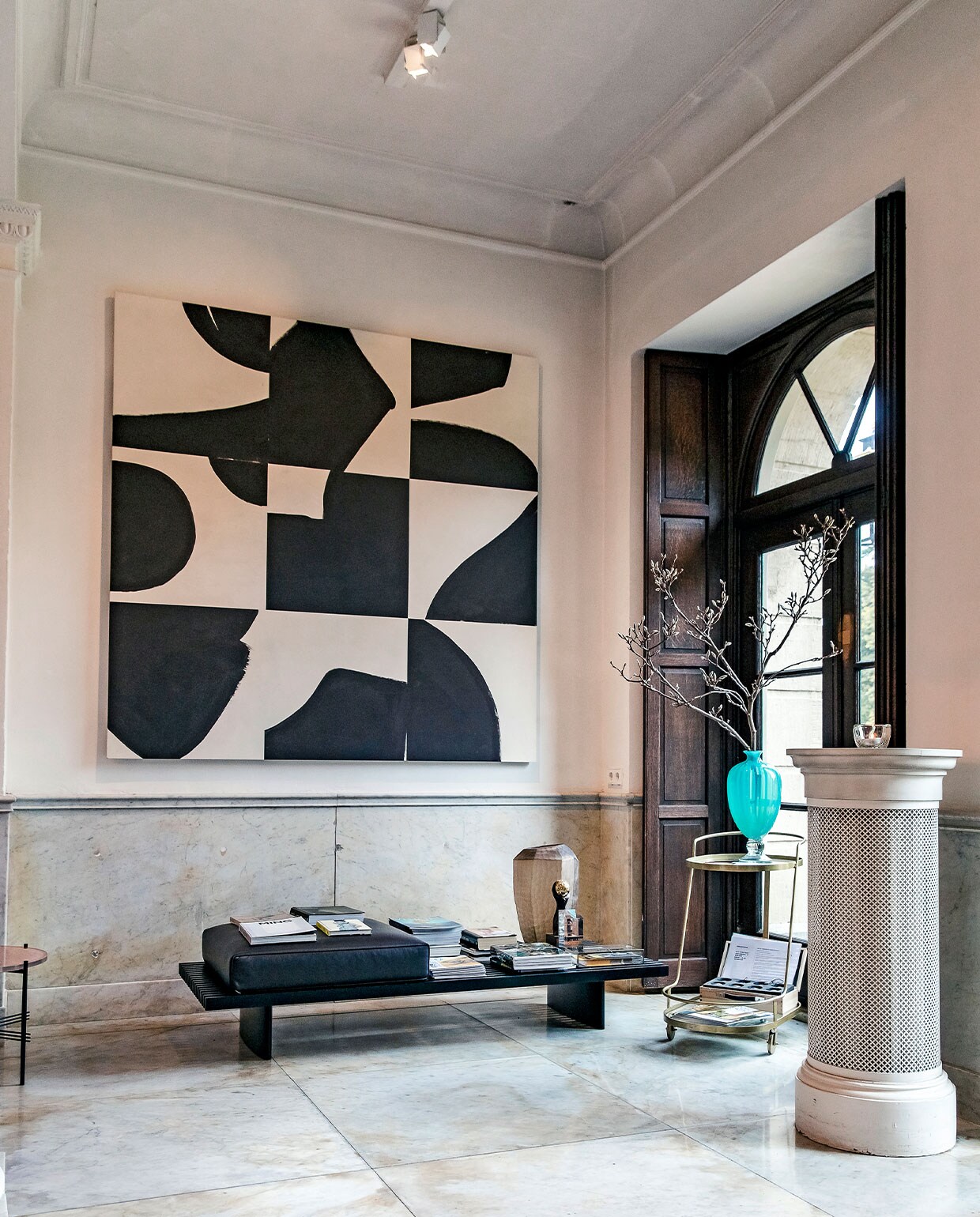 De entreeruimte van het hoofdhuis zet meteen de toon: klassieke elementen – zoals een marmeren vloer, lambrisering en donkere, houten luiken – in combinatie met moderne toevoegingen, zoals een strakke bank en XL abstract kunstwerk. vtwonen hotels bijlage 13-2020 | Fotografie Ernie Enkelaar  | Tekst Roos Stalpers en Fee van ’t Veen