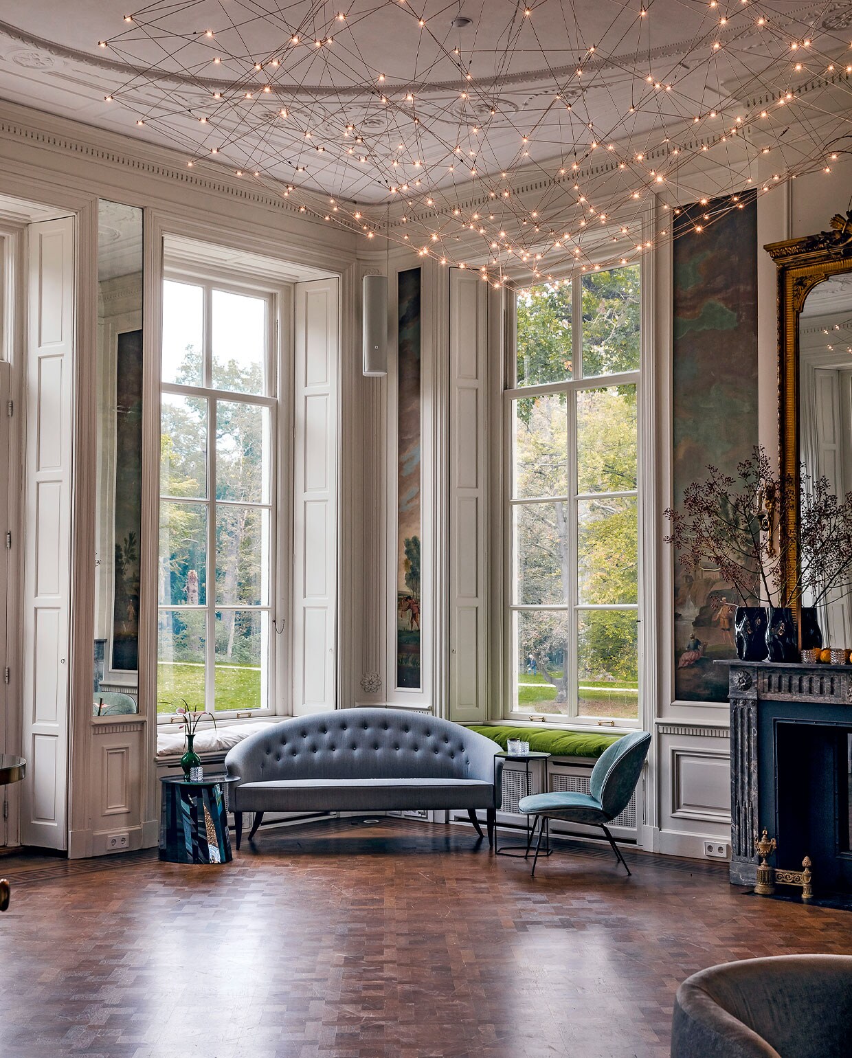 In de salon op de eerste verdieping is origineel geschilderd behang behouden. De luiken maken gordijnen overbodig, die zouden het beeld stoffig maken en het vrije uitzicht belemmeren. Sofa Paradise is een ontwerp van de Zweedse Kerstin Hörlin-Holmquist voor Gubi. vtwonen hotels bijlage 13-2020 | Fotografie Ernie Enkelaar  | Tekst Roos Stalpers en Fee van ’t Veen