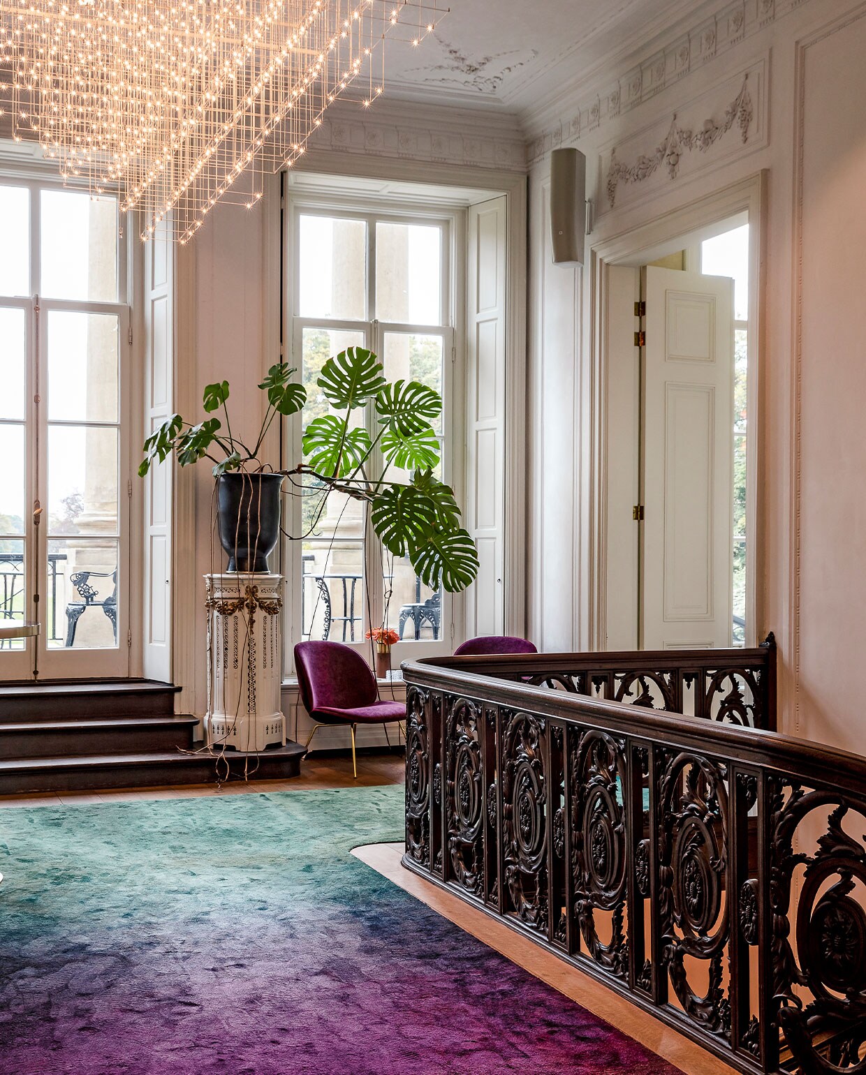 In het monumentale trappenhuis met donkere balusters, sierlijk stucwerk en plafondornamenten ontwierp Judith een loper met dégradé-effect, van hardroze naar groen. De krachtige kleuren zwakken het effect van het eikenhout af. Het spectaculaire, ijle lichtobject van Jan Pauwels maakt de balans tussen klassiek en modern compleet. vtwonen hotels bijlage 13-2020 | Fotografie Ernie Enkelaar  | Tekst Roos Stalpers en Fee van ’t Veen
