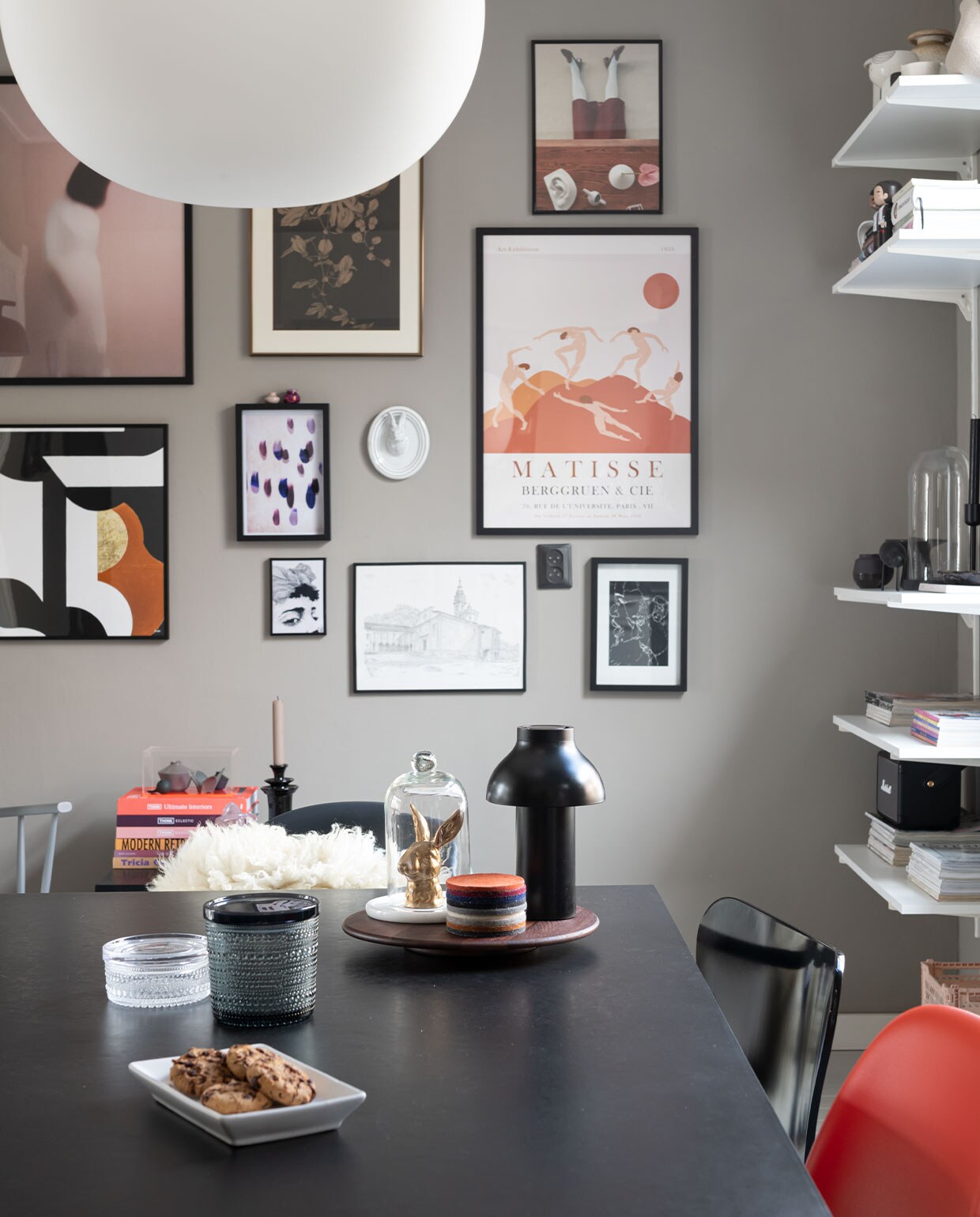 Stoel J110, wandlamp Hay, kussen zelfgemaakt. Hanglamp Glo Ball S2 van Flos. Vloerkleed en vitrinekist HKliving, minivaasjes Hella Duijs. Zwarte bijzetter Westwing, kandelaar Day. Konijn Vintage Fever, onderzetters Nio &amp; Elva. Potten Iittala. Wandlamp Ambit van Muuto. Kunst v.l.n.r.: print vrouw Mia Wallace via Ruben Ireland, H&amp;M. Haas papier-maché Babettes Wereld, tegel Studio Job van Koninklijke Tichelaar, posters vrouw en print druppel en gezicht Juniqe. Minivaasjes op lijst van bevriende kunstenaar. Print roze vrouw Gurille Design, grafische print Part 2 Terra van Atelier Andrea. Passiebloem van Anton Pieck uit ouderlijk huis. Keramieken hazenkop Des Pots. Print Matisse Pstr studio. Tekening Zwitserse kerk door plaatselijke kunstenaar. Print Rechtszaak van Studio Abeelen. Muurverf Authentic Grey van Flexa. Eettafel en zwarte lamp Hay,. Konijn Vintage Fever. Panton Chairs van Vitra, vacht sheepy.cc. vtwonen 13-2021 | styling Sharon Roest | fotografie Caroline Martinot | tekst Monique van der Pauw