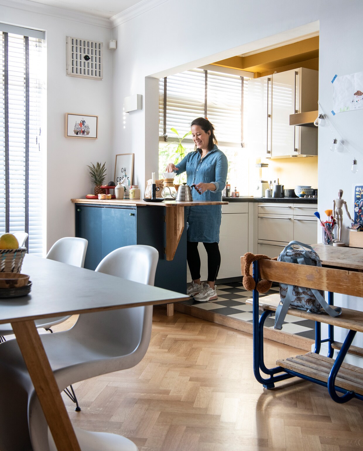 Keuken Siematic, muurverf India Yellow van Farrow &amp; Ball via De Ru. Vloertegels van winkel die niet meer bestaat. Kast op maat laten maken door een timmerman, zelf geverfd in kleur RAL 5008. Kastknoppen Oyoy. Wandlamp zat al in het huis. Oh Crêpe-poster Sissy-Boy, illustratie Clémentine Latron. Hoge pot souvenir uit Italië, mosterdpot Vendejo. Koffiepot Chemex, kandelaar souvenir uit België, waterkan Hario, fruitplateau Vitra, schaaltje knutselwerk Magalie, theepot Bredemeijer, schalen op aanrecht van Chinese toko. Tafel CPH30 van Hay, borden op tafel Serax, rieten mand souvenir uit Sardinië. Panton-stoel en Eames DSR-stoel Vitra. Vintage schoolbureau Marktplaats, tas Artis, potloden Van Gogh Museum. Ledlichtslinger Edison van Kikkerland. Overig onbekend. vtwonen 13-2021 | Productie Insidehomepage | Styling Kim Timmerman | Fotografie Louis Lemaire | Tekst Inge van Lieshout | Tekstbewerking Mariska Keus
