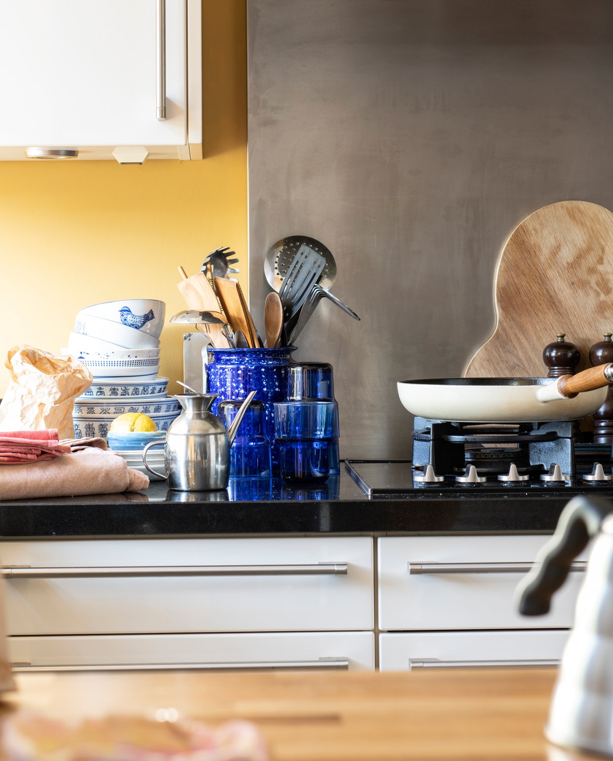 Keuken Siematic, muurverf India Yellow van Farrow &amp; Ball via De Ru. Glazen en plank Iittala. Kommen van een Chinese toko. Pot Arket. Schaaltjes &amp;klevering, kleinste schaaltje zelf geboetseerd. Pan Le Creuset. vtwonen 13-2021 | Productie Insidehomepage | Styling Kim Timmerman | Fotografie Louis Lemaire | Tekst Inge van Lieshout | Tekstbewerking Mariska Keus