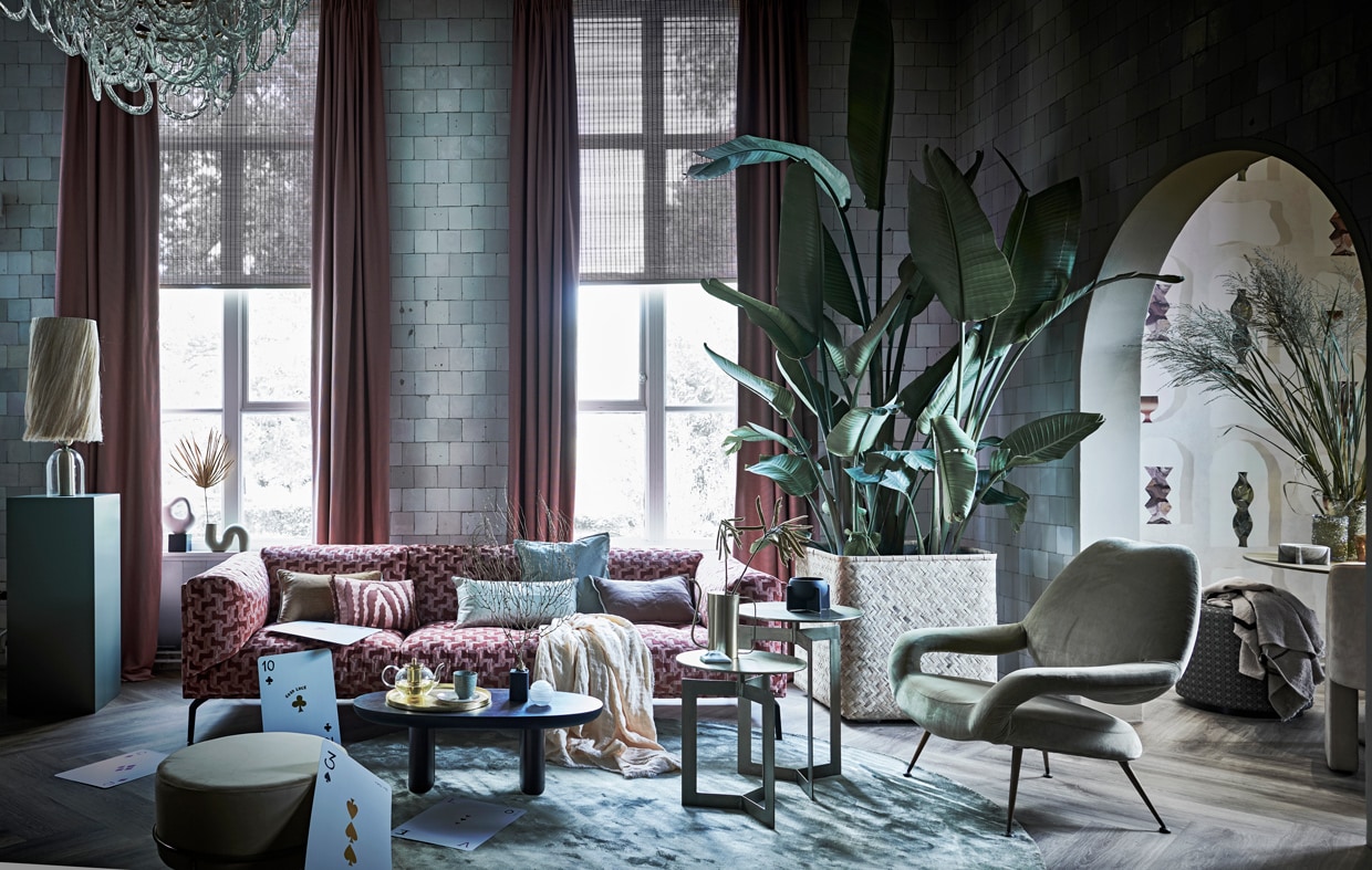 Glanzend kussen op bank € 135,-, bruin kussen links op bank € 338,- (homestede.nl). Lampenkap Boho met losse abaca-vezels, 28×56 cm (Øxh) € 179,-, vaas links in raam € 39,95, roze kussen links € 34,95, roze bord op tafel € 29,95, plaid rechts op kruk € 74,95 (hkliving.nl). Lampenvoet € 135,95, glazen theepot € 83,-, goudkleurige gieter € 41,40, groene glazen vaas rechts, maat M € 89,-, gele vaas rechts, maat L € 98,-, marmeren schaal met voet rechts € 95,-, goudkleurige bijzettafels Nyasa, set van twee € 499,- (nordal.eu). Groene polyester tafel rechts, 130 cm (Ø) € 1499,- (householdhardware.nl). Lederen stoel € 3061,-, groene loungestoel € 3267,- (covanderhorst.nl). Gele poef met goudkleurige voet Daisy van Lifa Living, 55×35 cm (Øxh) € 59,95, rond vloerkleed Ravel van Bepure Home, 250 cm (Ø) € 499,-, goudkleurige schaal Salt &amp; Pepper van Palace, 37 cm (Ø) € 39,95, linnen plaid op bank van HKliving, 140×220 cm (bxl) € 95,- (vtwonen.nl). Sculptuur op zwarte voet € 29,99 (hm.com). Roze 3-zitsbank, 250x95x74 (bxdxh) € 4315,-, ovale houten tafel, 90 cm (b) € 750,-, zwart bakje € 90,- (allestedlund.com). Behang Asteré rechts, 1×10 m (bxl) per rol € 330,-, kruk met print rechts, prijs op aanvraag, gordijnen op maat gemaakt, stof Andrew per meter € 77,-, goudkleurig koraal op zwarte voet € 149,-, witte sierbol (bakje) € 49,-, witte wierrookhouder L’Object € 99,-, groene pilaar € 495,- (luxerybynature.nl). Kaartspel getekend door Demi Hoekstra (drukkerij-flora.nl). Planten en takken prijs op aanvraag (waterdrinker.nl). vtwonen 13-2021 | styling liza Wassenaar | fotografie Sjoerd Eickmans | assistentie Kula van den Broek, Demelza Krens, Philine Jansen