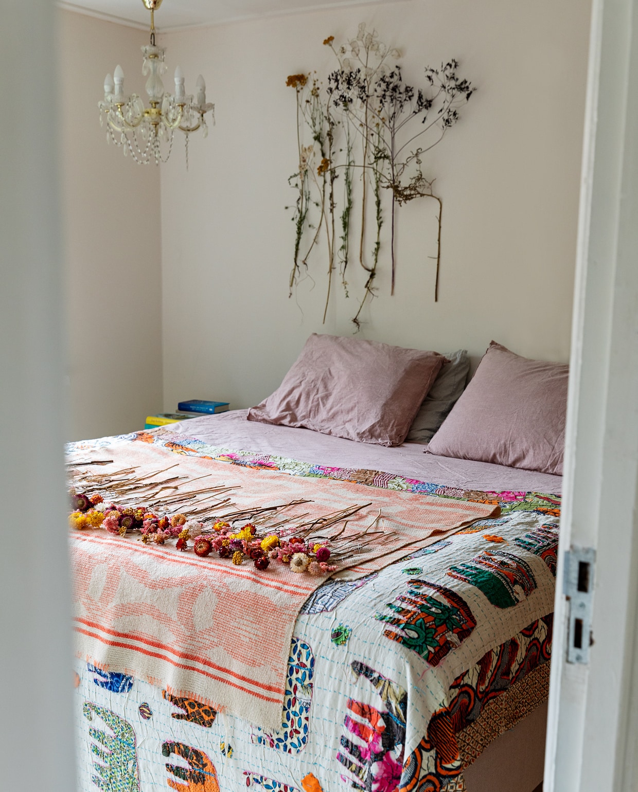 Bed en beddengoed Ikea. Deken met olifanten souvenir uit India. Kroonluchter Sissy-Boy. Roze plaid met gedroogde bloemen en verzameling gedroogde planten aan muur Loesje van Herp. vtwonen 13-2021 | styling Ilona Jongepier | fotografie Dana van Leeuwen