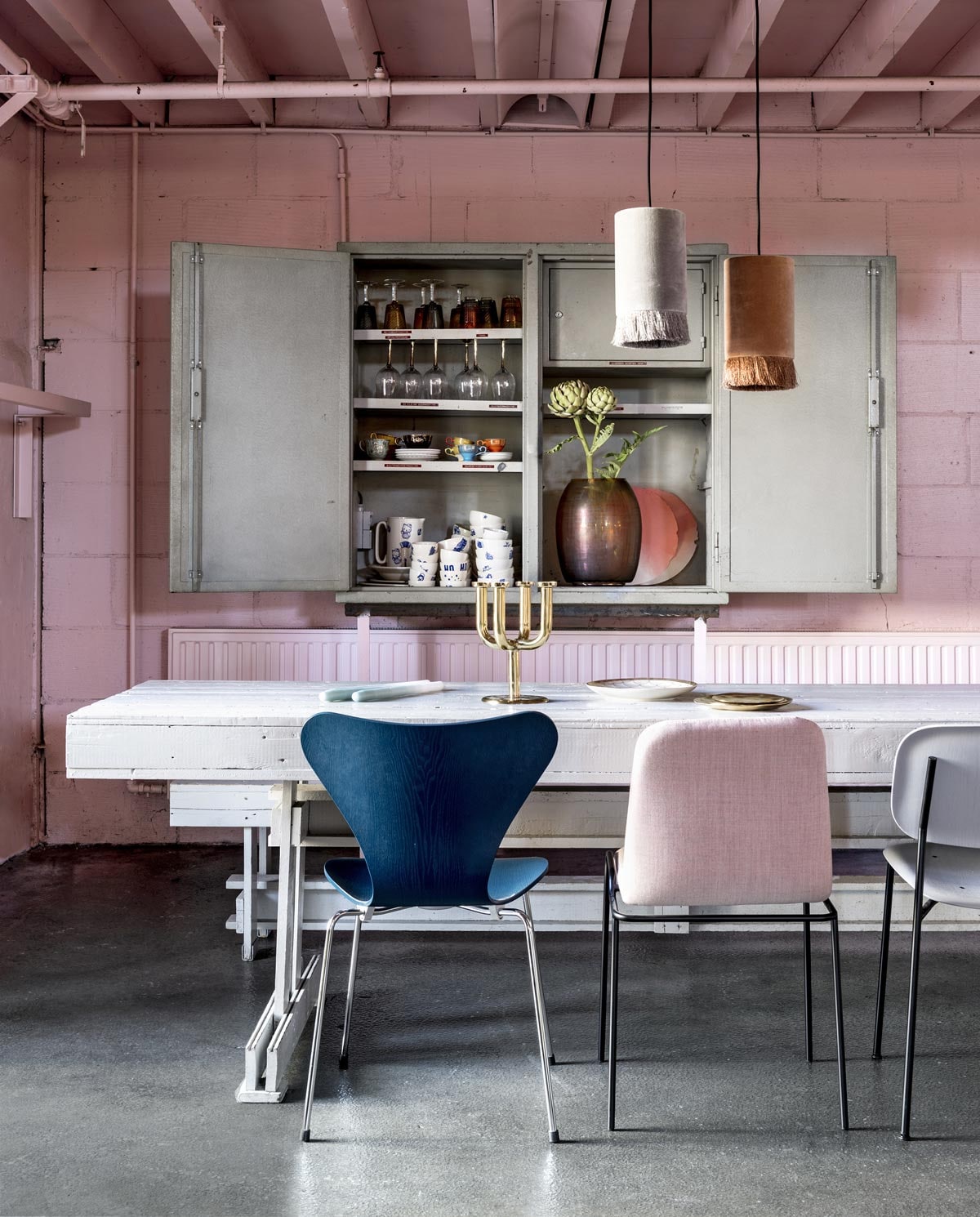 Tafel, bank in samenwerking met Piet Hein Eek (Social Label). Op tafel messing kandelaar (Pols Potten). Gouden bord van &amp;Klevering (vtwonen.nl). Fritz Hansen series 7 vlinderstoel ontworpen door Arne Jacobsen, roze gestoffeerde stoel van Ligne Roset, grijze stoel Soft Edge Dining Chair van Hay (Mister Design). Lampen van Madam Stoltz (deens.nl). Fabriekskast (Neef Louis). In de kast keramiek met blauw dessin uit 27-delig servies in samenwerking met ontwerper Edwin Vollebergh (Social Label). Wijnglazen met gouden voet van Bloomingville (vtwonen.nl). Gekleurde kop-en-schotels, gekleurde glazen, gekleurde wijnglazen, glazen vaas met olieachtige glans (Pols Potten). Overig privébezit. vtwonen 12-2018 | Fotografie Stan Koolen | Styling Marianne Luning | M.m.v. Social Label Den Bosch