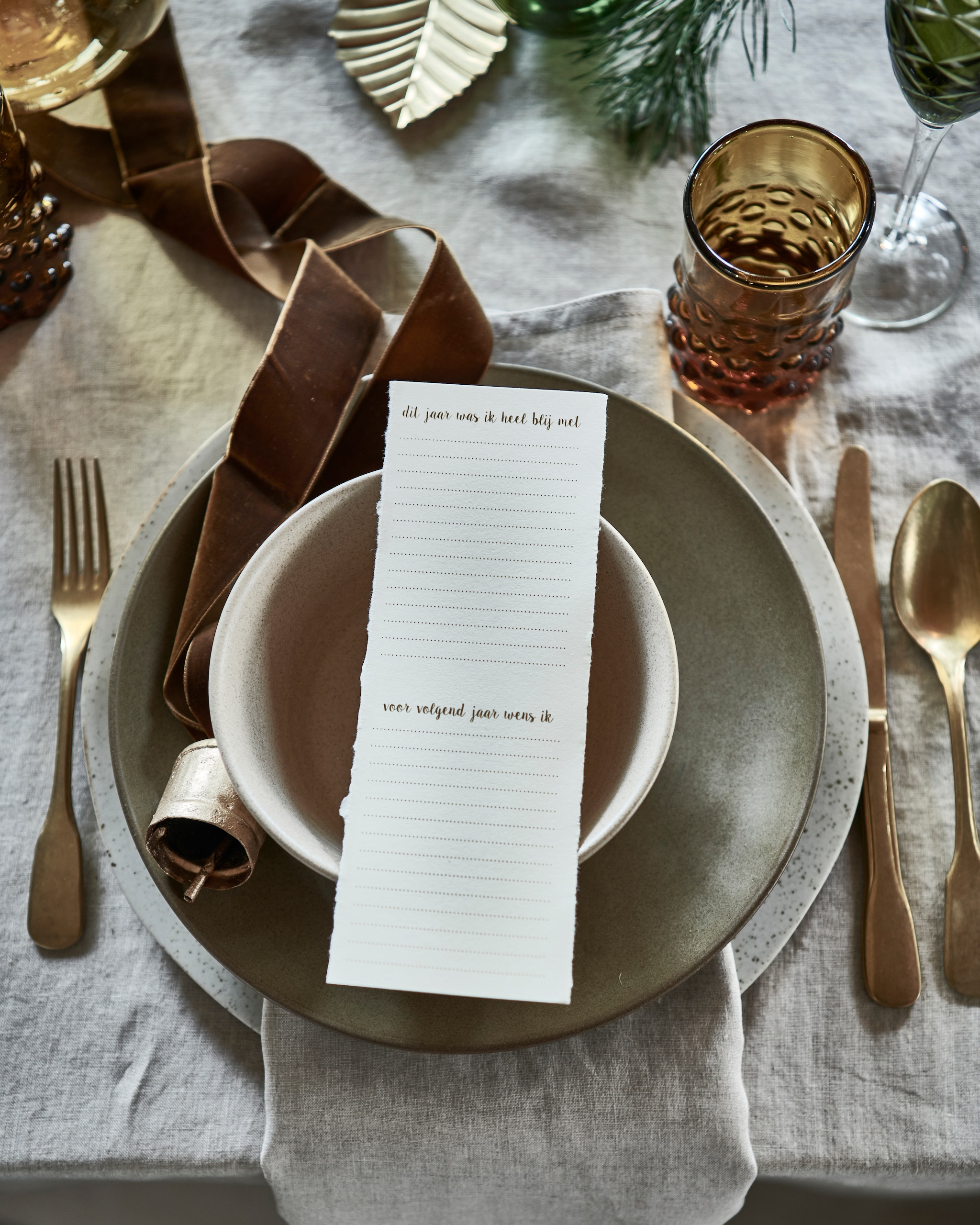 linnen tafelkleed € 39,99, servet, set van 2 € 9,99 (hm.com). Groen bord € 27,95, beige kom, groen ovaal bord, alles aardewerk van Studio Ro Smit (factor-ij.amsterdam). Beige bord € 25,- (nordal.eu). Groen champagneglas, set van 6 € 160,- (polspotten.nl). Gouden kerstbal in vorm van bel, set van 2 € 15,-, gouden blad, set van 3 € 6,- (bungalow.dk). vtwonen 12-2021 | styling Danielle Verheul | Fotografie Sjoerd Eickmans | Tuin van Judith (groenstylist), assistentie Niels Kist, Kula van den Broek