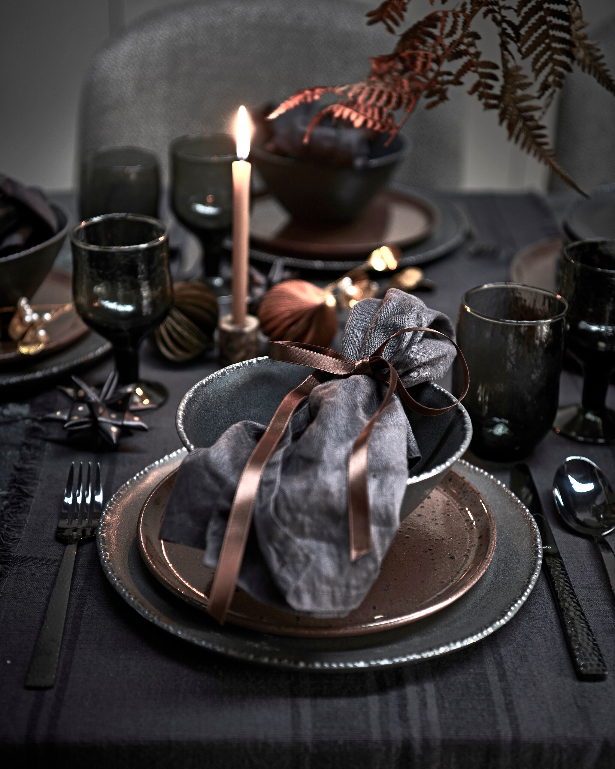 Bloemen, prijs op aanvraag (tuinvanjudith.wordpress.com). Tafelloper € 9,99, zwarte borden, per stuk € 12,99, zwarte kommen, per stuk € 9,99, servetten, set van twee € 9,99 (hm.com). Grijze water- en wijnglazen, per stuk vanaf (anna-nina.nl). Bestek van Amefa, 24-delige set € 55,65, grijs gestoffeerde stoelen van Dutchbone, per stuk € 232,35 (vtwonen.nl). Gespikkeld bruin bord, marmeren kandelaar € xxx, lange dunne kaars, kerstbal ster (letoile.store). Metalen mistletoe, set van 2 € 17,50, papieren kerstballen, per stuk € 3,- (bungalow.dk). vtwonen 12-2021 | styling Danielle Verheul | Fotografie Sjoerd Eickmans | Tuin van Judith (groenstylist), assistentie Niels Kist, Kula van den Broek