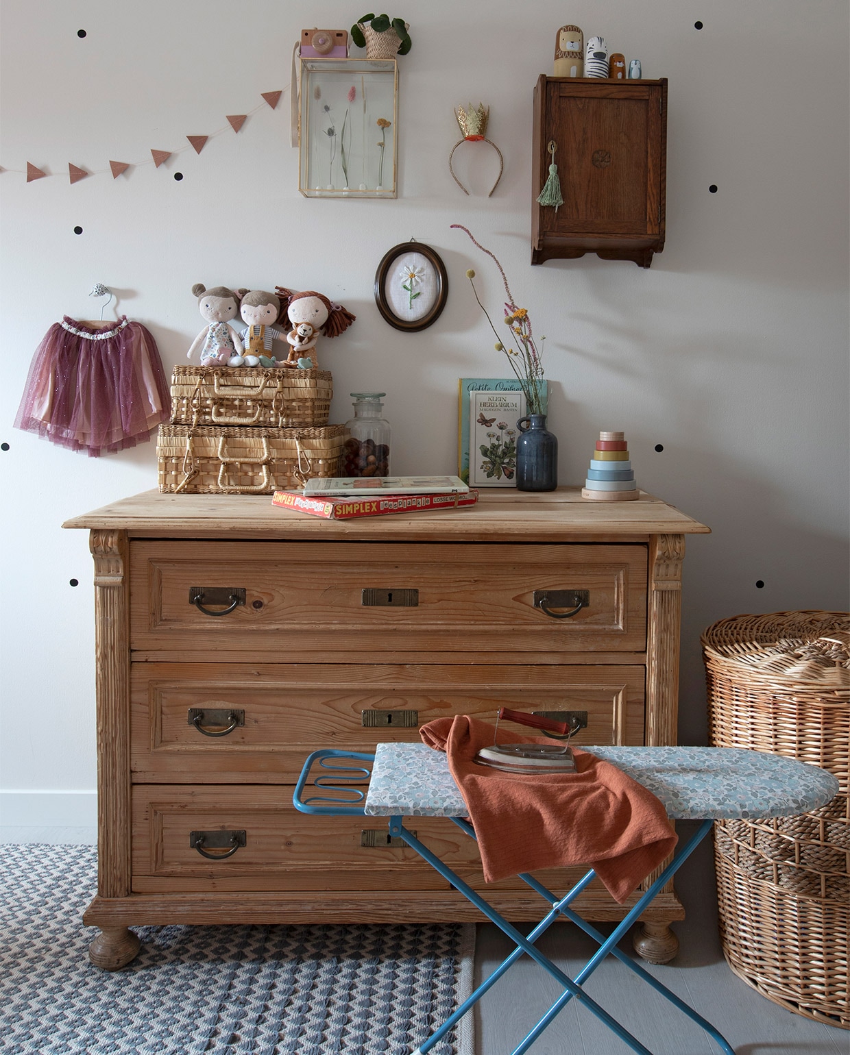 Commode en mand Marktplaats. Glazen kast Kwantum. Wandkast uit een antiekwinkel. Vloerkleed GoRound Interior. Muurstickers zwarte stipjes online gevonden. Slinger Søstrene Grene. Koningsdag- diadeem Hema. Matroesjka-dieren, poppen en stapeltoren Little Dutch. Rok Zara. Rieten koffers en zwarte lijst kringloopwinkel. Borduurwerk zelfgemaakt. Strijkplank rommelmarkt. vtwonen 08-2021 | fotografie Macha Gutlich
