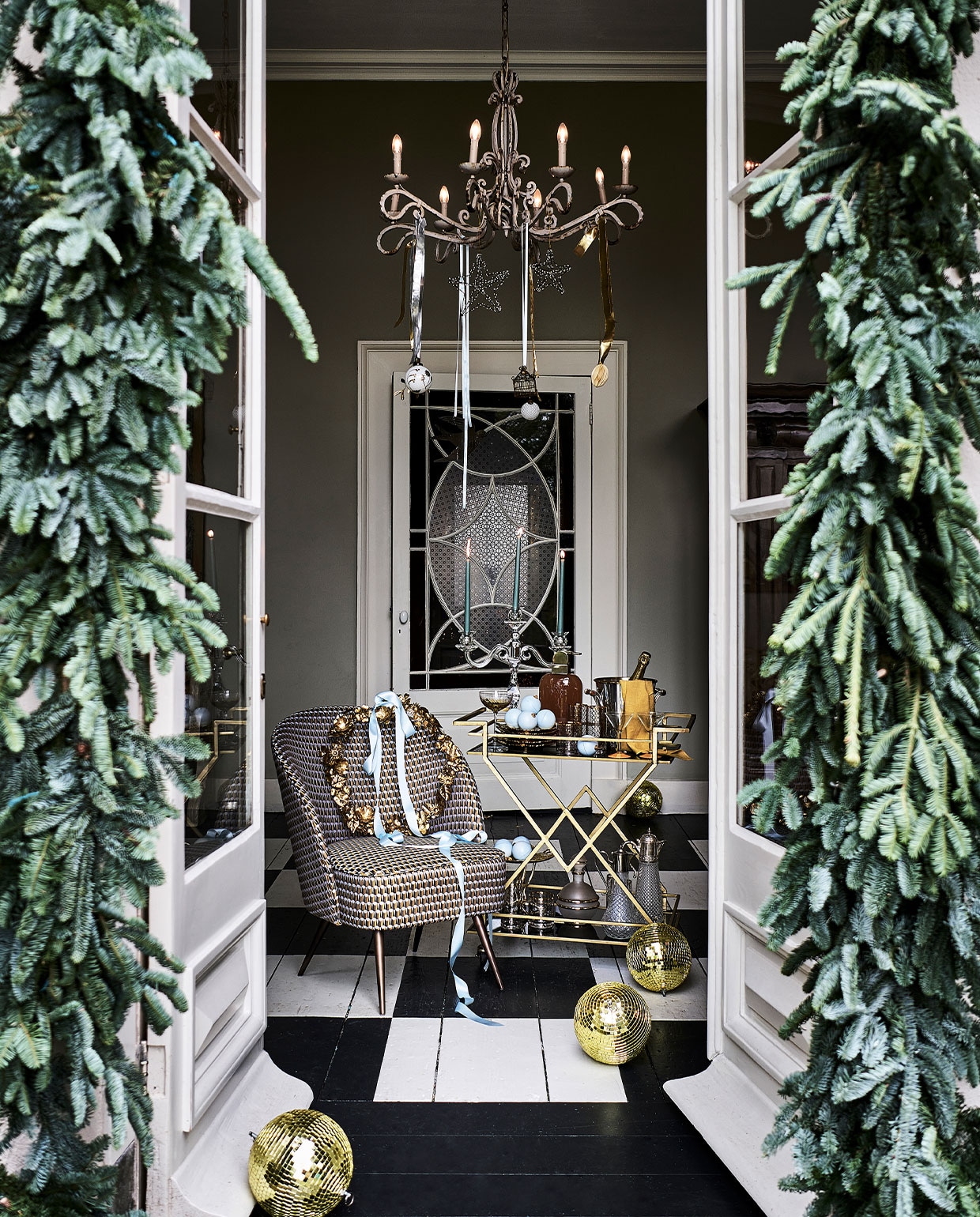 Trolley € 599,-, glazen met goudkleurig dessin vanaf € 12,95, cocktailglas links € 12,95, glazen kandelaar € 238,- (nordal.eu). Bloemstyling, p.o.a. (judithslagter.nl). Goudkleurige discoballen, per stuk € 32,50 (spektakelwonen.nl). Blauwe chocolade kerstballen, per stuk € 7,95 (toutpatisserie.nl). Fauteuil € 725,-, borden in bladvorm, per stuk € 32,- (allestedlund.com). Servet, set van 2€ 12,-, papieren ei in kroonluchter, maat XL € 12,-, krans € 47,- (bungalow.dk). Wijnkoeler € 280,- (wildschut-antiques.com). Cocktailglazen met gele voet, per stuk € 10,-, drankfles € 95,-, kannen rechtsonder op trolley, per stuk € 65,-, drankfles mat glas met goudkleurige rand € 35,- (harlequin-lisse.biz). Blauwe kaarsen, set van 2€ 1,99 (hm.com). Plateau € 159,- (luxurybynature.nl). Handgemaakte en gerecyclede kerstballen in kroonluchter en op trolley, vanaf € 6,95 (weldaad.com). Lint privébezit. Droogbloemen en kersttakken (waterdrinker.nl). vtwonen 12-2021 | styling Liza Wassenaar | fotografie Sjoerd Eickmans | assistentie Kula van den Broek, Sanne Ketelaar | bloemstyling Judith Slagter