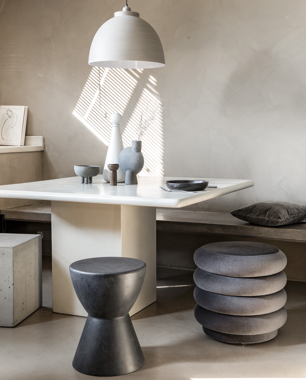 Eettafel van de kringloopwinkel, in beton-ciré gezet, prijs op aanvraag (betoncirenederland.nl). Vierkante kruk van beton (debetonfabriek.nl). Kruk van fiberclay, antracietgrijs, ook voor buiten (woood.nl). Poef fluweel (fermliving.com). Vaasje Sphere mini, vaasje Sphere medium (casagitane.com). Witte fles met dop Muses Era, zoutmolen Drupe mill, in smoked ash (fermliving.com). Hanglamp in betonlook (karwei.nl). Bord Black Pottery (couleurlocale.eu). Kussen bruin fluweel, 45×45 cm (loods5.nl). Bestek privébezit. vtwonen 1-2020 | styling Marlies Does | fotografie Peggy Janssen