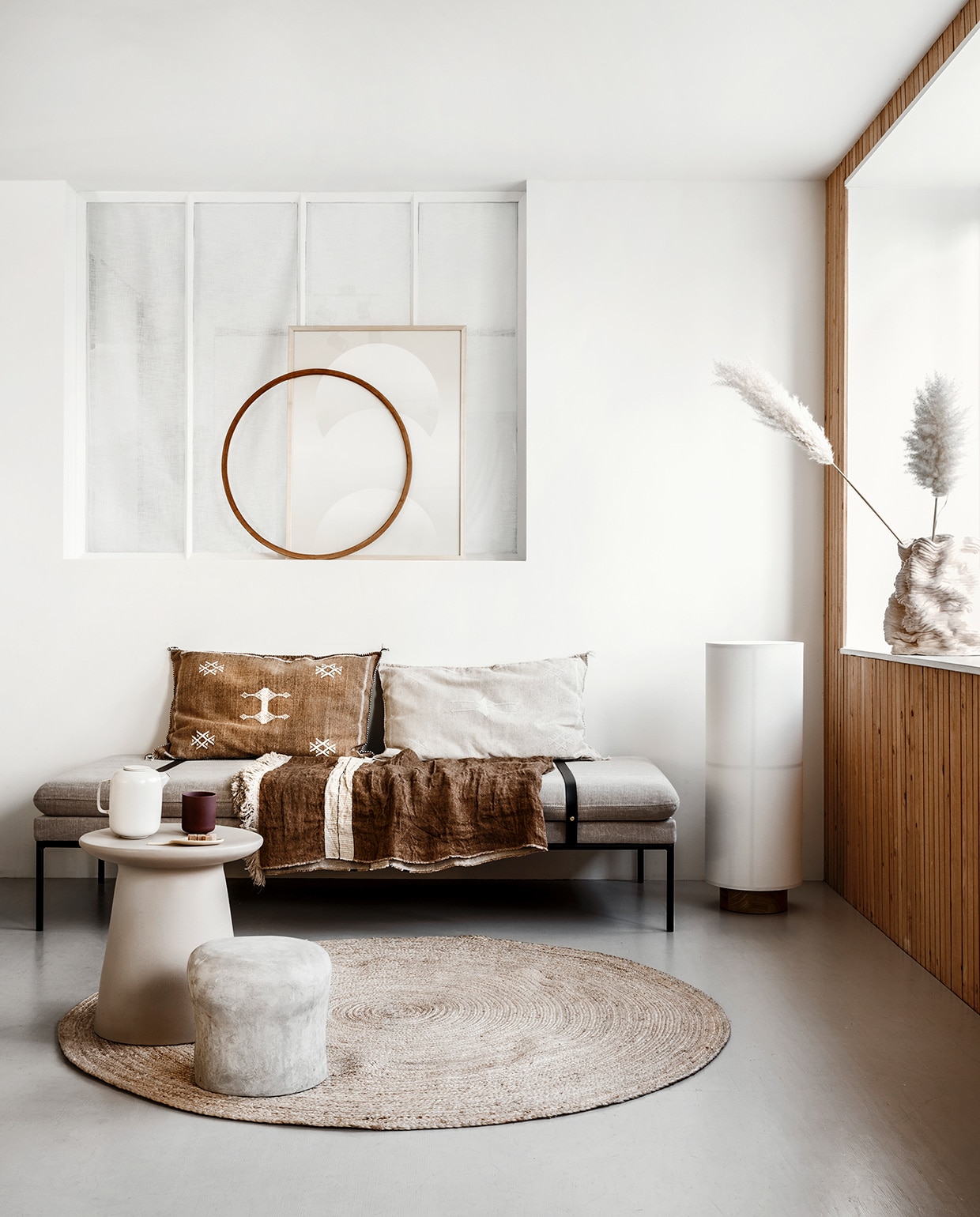 Daybed van Ferm Living met leren banden(kolkenkolk.nl). Rieten mat van Nordal, Ø 150 cm (vtwonen.nl). Vloerlamp Hashira (menudesignshop.com). Bijzettafel van keramiek (boer-staphorst.nl). Betonnen kruk van FCK (serax.com). Kussens met fijne borduursels (zenzaliving.com). Linnen doek Bruges stripe (libeco.com). Grafische print, handgemaakte vaas (2222studio.com). Houten cirkel privébezit. vtwonen 05-2020 | styling Marianne Luning | fotografie Stan Koolen