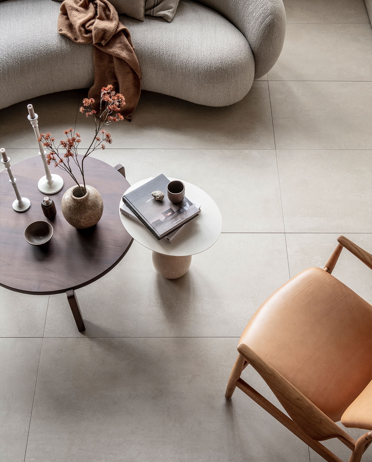 Vloertegel Raw in kleur Sand, 60×120 cm, per m² € 69,-. | M.m.v. justhaasnoot.nl (staande lamp, bank Julep van Tacchini, salontafel Guéridon Bas van van Vitra, witte bijzettafel Lato van &amp;Tradition, fauteuil van hout met leer van House of Finn), zarahome.com (witte metalen kandelaars, stenen vaas), suhka.nl (textielkunstwerk, kom en mok). Overig privébezit. vtwonen 11-2021 | productie Tanja Saarberg |  styling Kim van Rossenberg | fotografie Sjoerd Eickmans