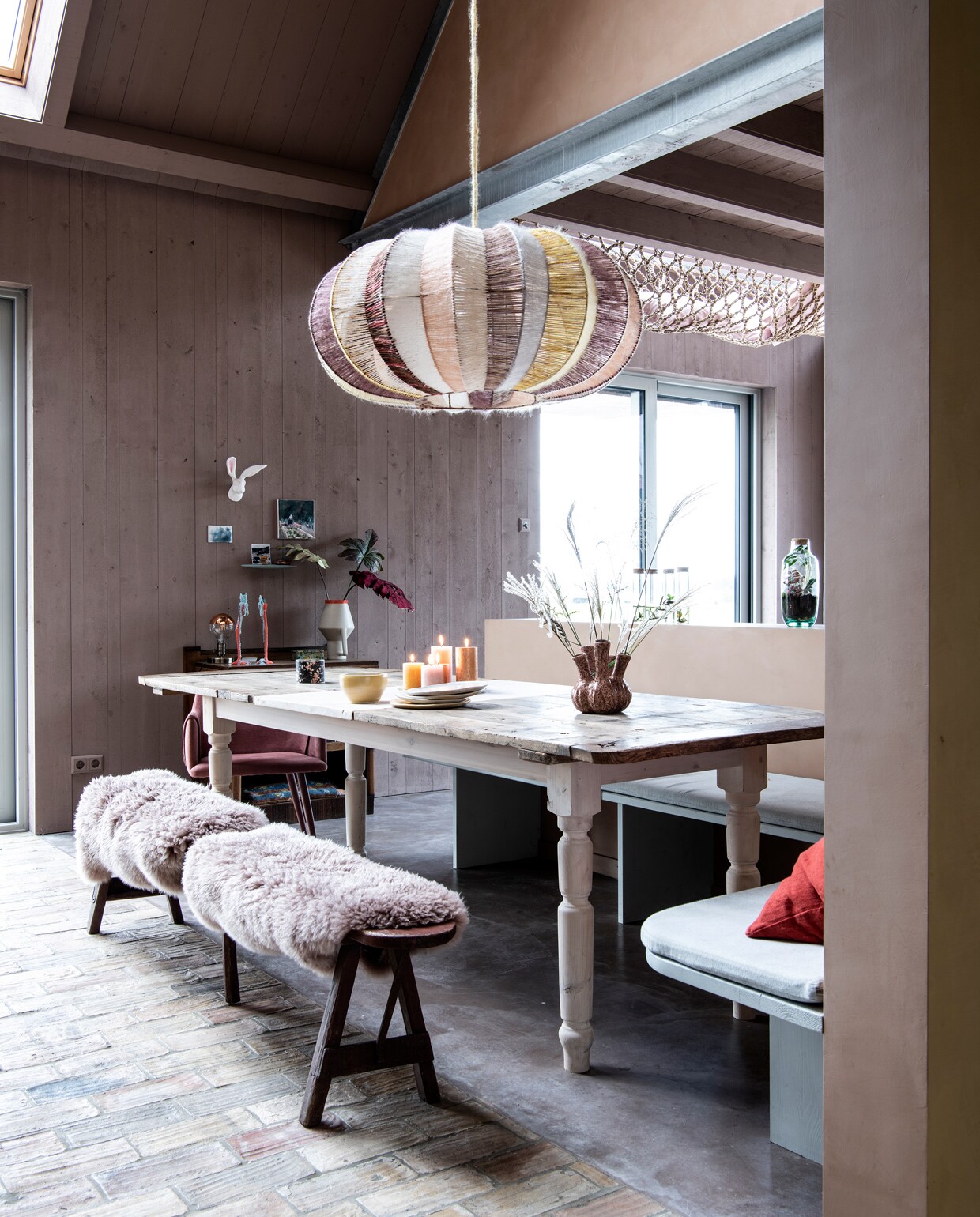 Hanglamp eigen ontwerp van Larissa, gemaakt door HeinsHome. Tafel zelfgemaakt van een oude deur, vergroot met tussenstuk. Onderstel Van Dijk &amp; Ko. Hoekbank maatwerk, in verfttint Soft Asparagus van Pure &amp; Original. Houten bank Marktplaats. Schapenvachten Ikea. Vaas op tafel lokale bloemenzaak. Schaal en borden keramist Loeke Pam. Kuipstoel Fonq. Rood kussen Wehkamp. Zitkussen hoekbank van recycle-denim via Annemieke Koster. vtwonen 11-2021 | styling Esther Jostmeijer | productie Insidehomepage | fotografie Louis Lemaire tekst Inge van Lieshout | tekstbewerking Sunna Borghuis